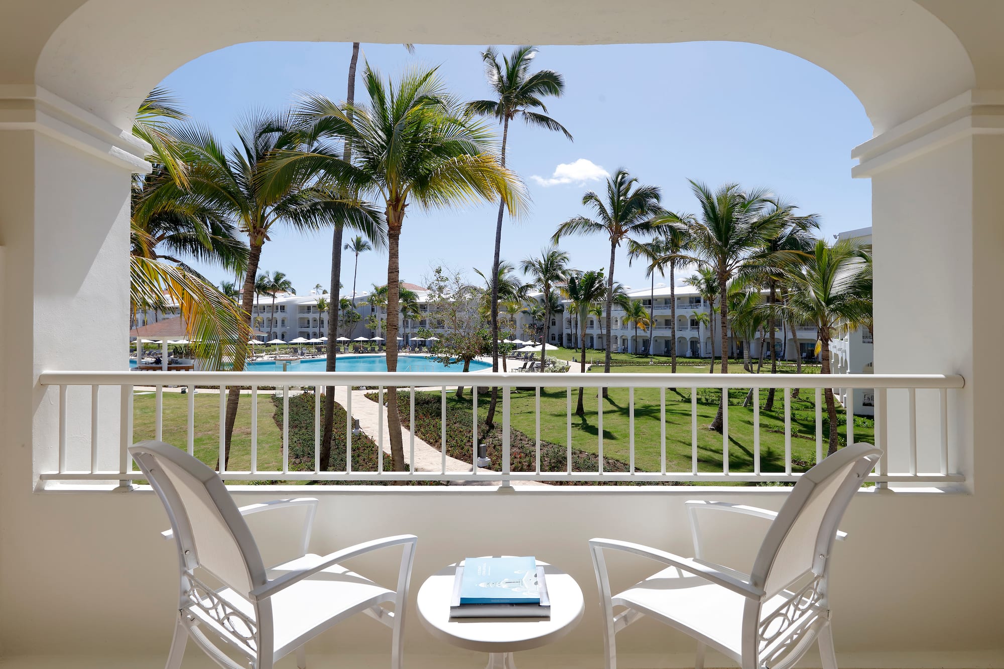 a balcony with chairs and a table and a pool in the background