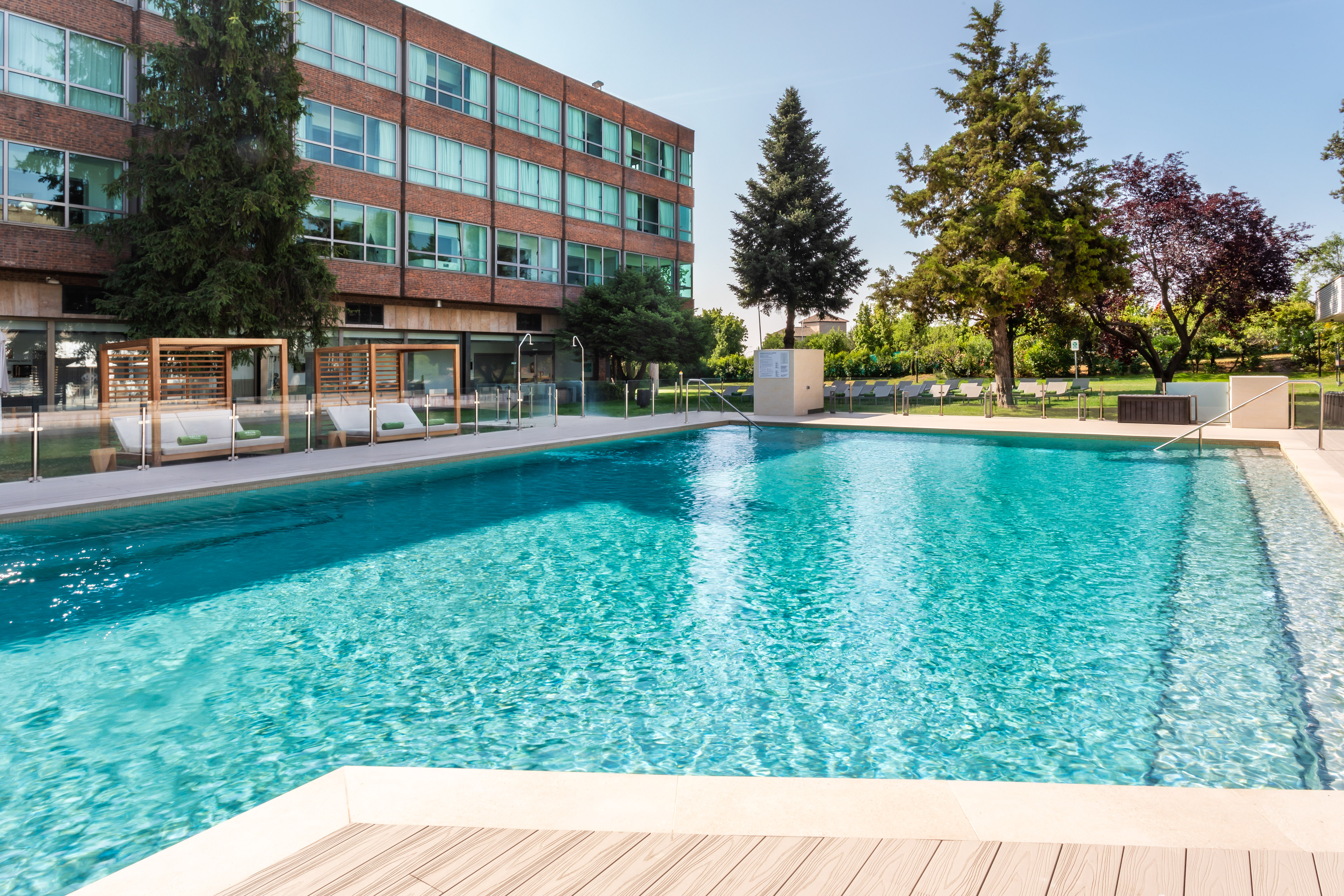Hotel outdoor swimming pool with turquoise water, brick facade, and cabanas.