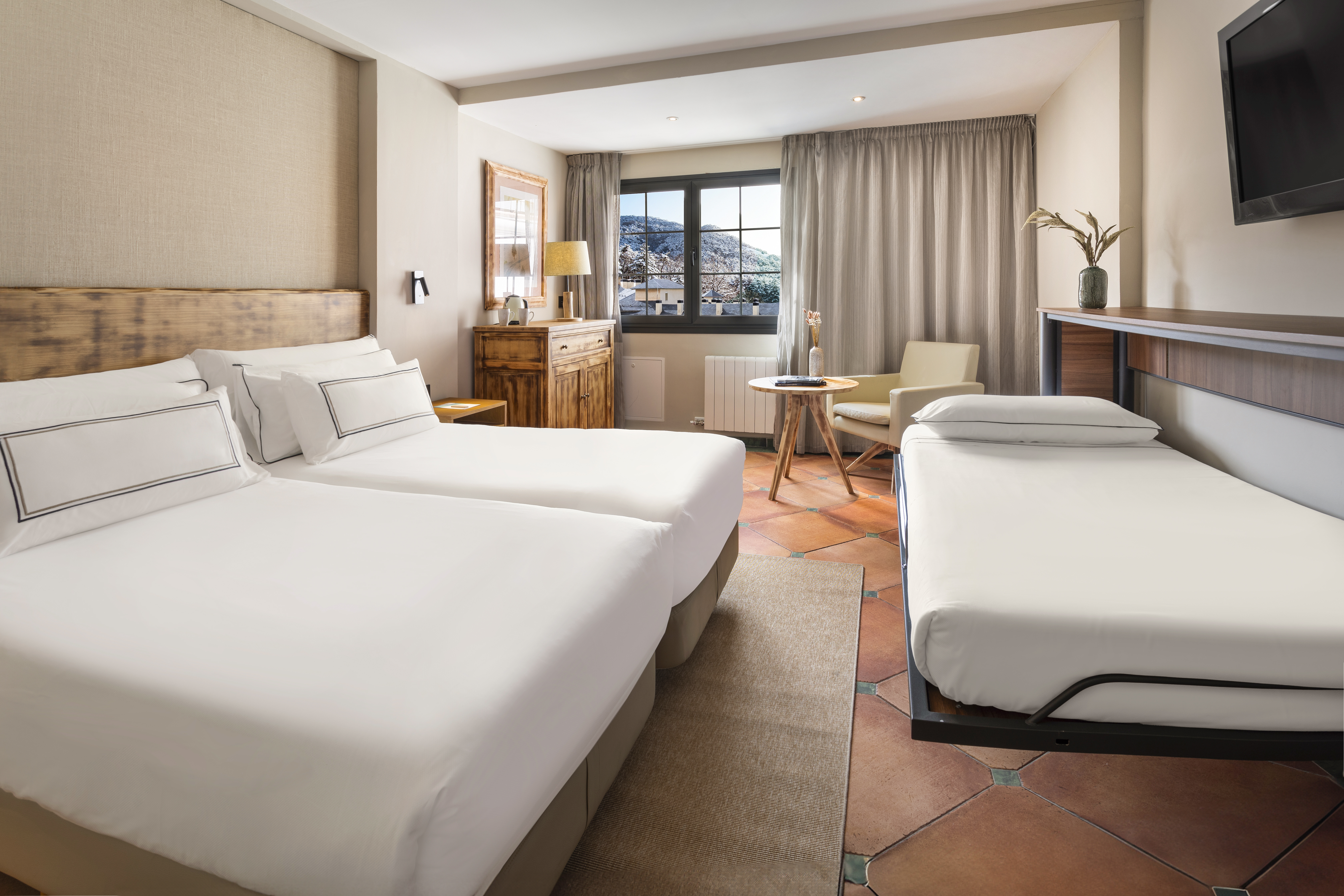 Hotel room with twin beds, extra bed, terracotta floor, and mountain view.