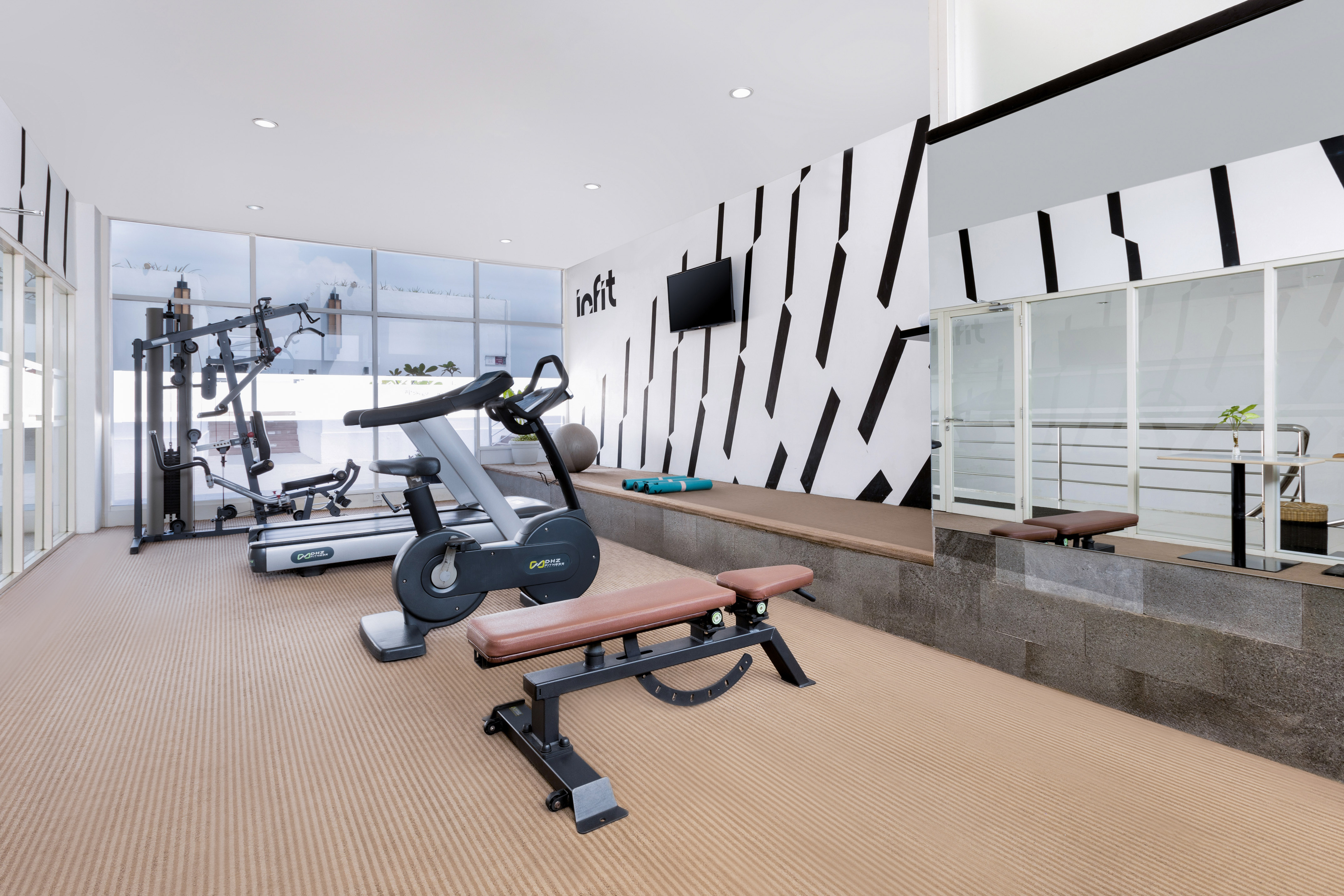 Modern gym with treadmill, stationary bike, weight bench, and large windows.