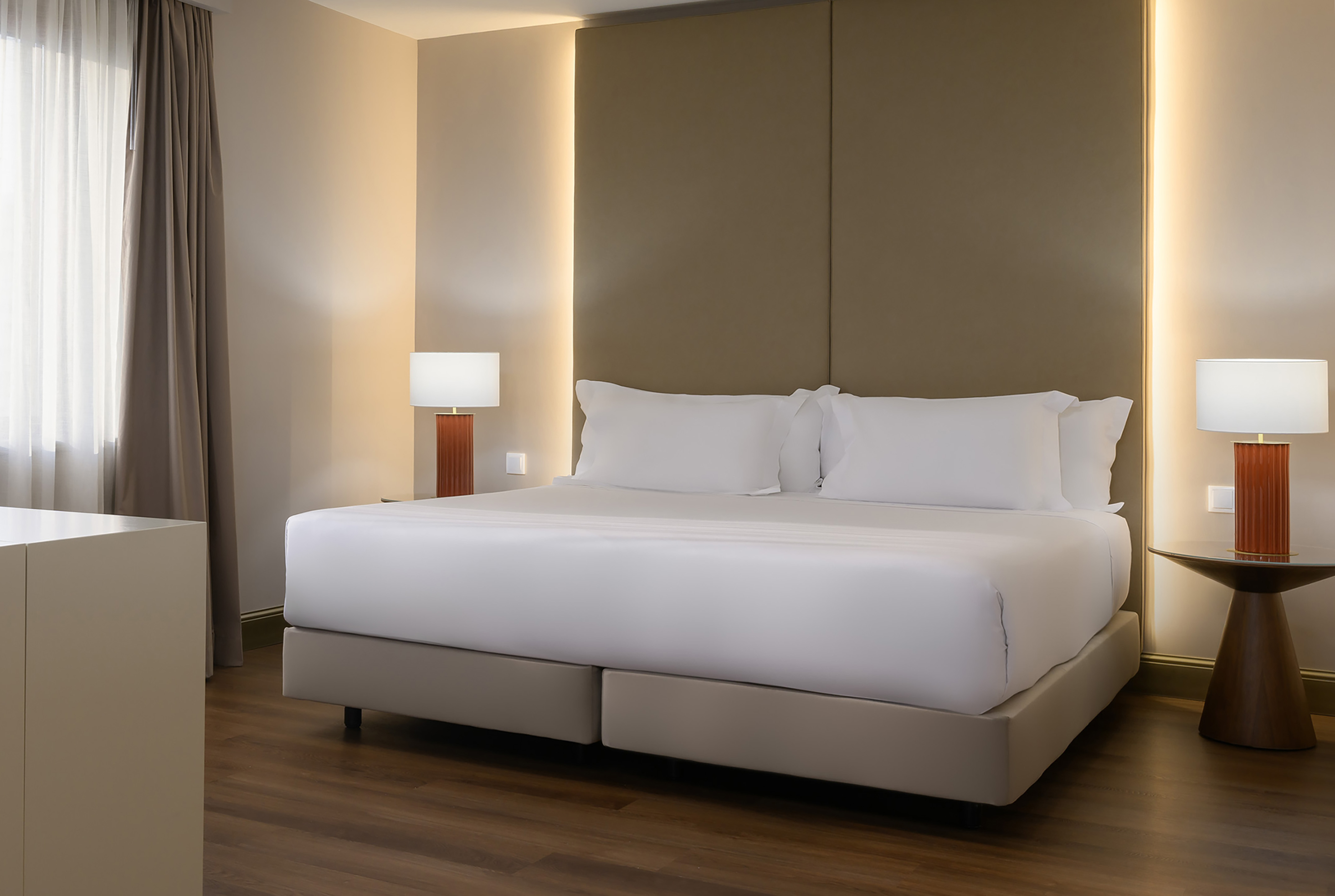 Luxurious hotel bedroom with large bed, padded headboard, and ambient lighting.