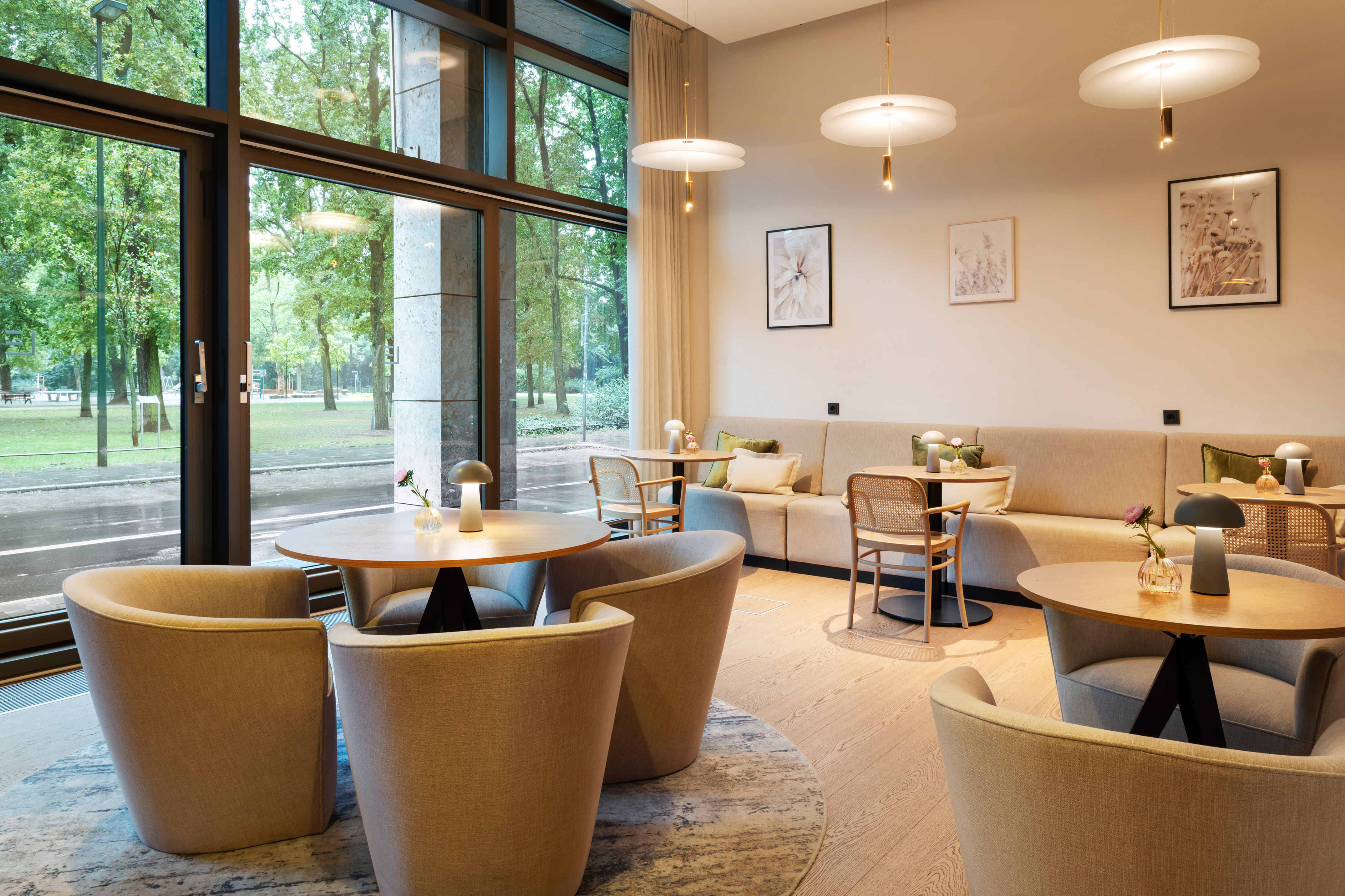 Modern hotel lounge with park view, comfy seating, tables, stylish lighting.