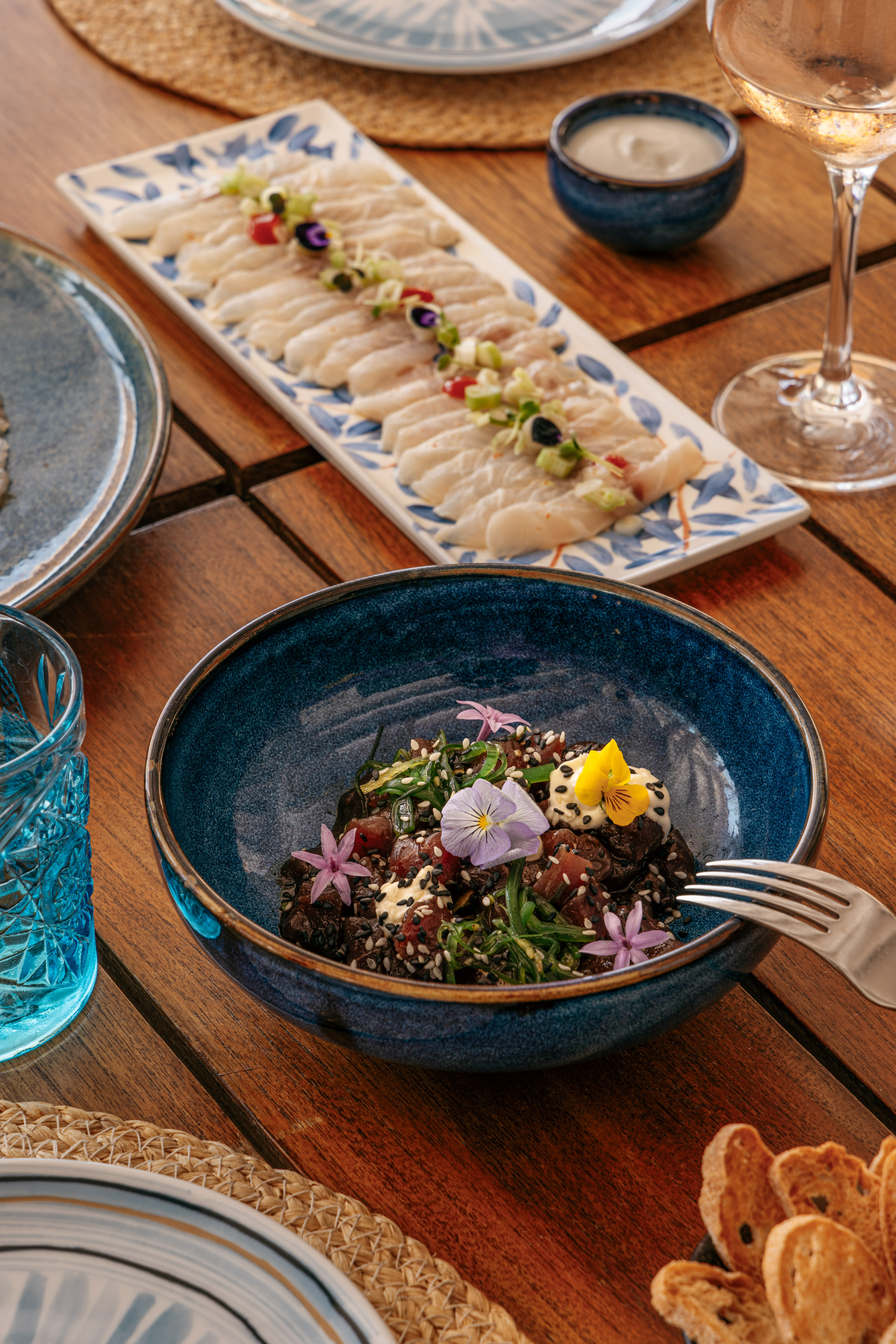 Tuna poke bowl with edible flowers, white fish carpaccio on wooden table.