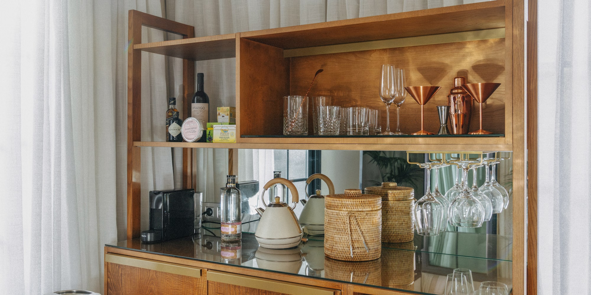 Wooden minibar cabinet with bottles, cocktail glasses, Nespresso, and kettle.