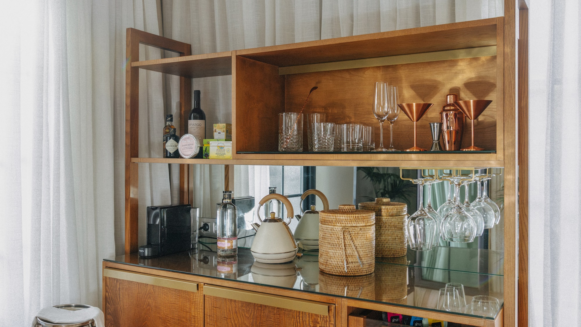 Wooden minibar cabinet with bottles, cocktail glasses, Nespresso, and kettle.