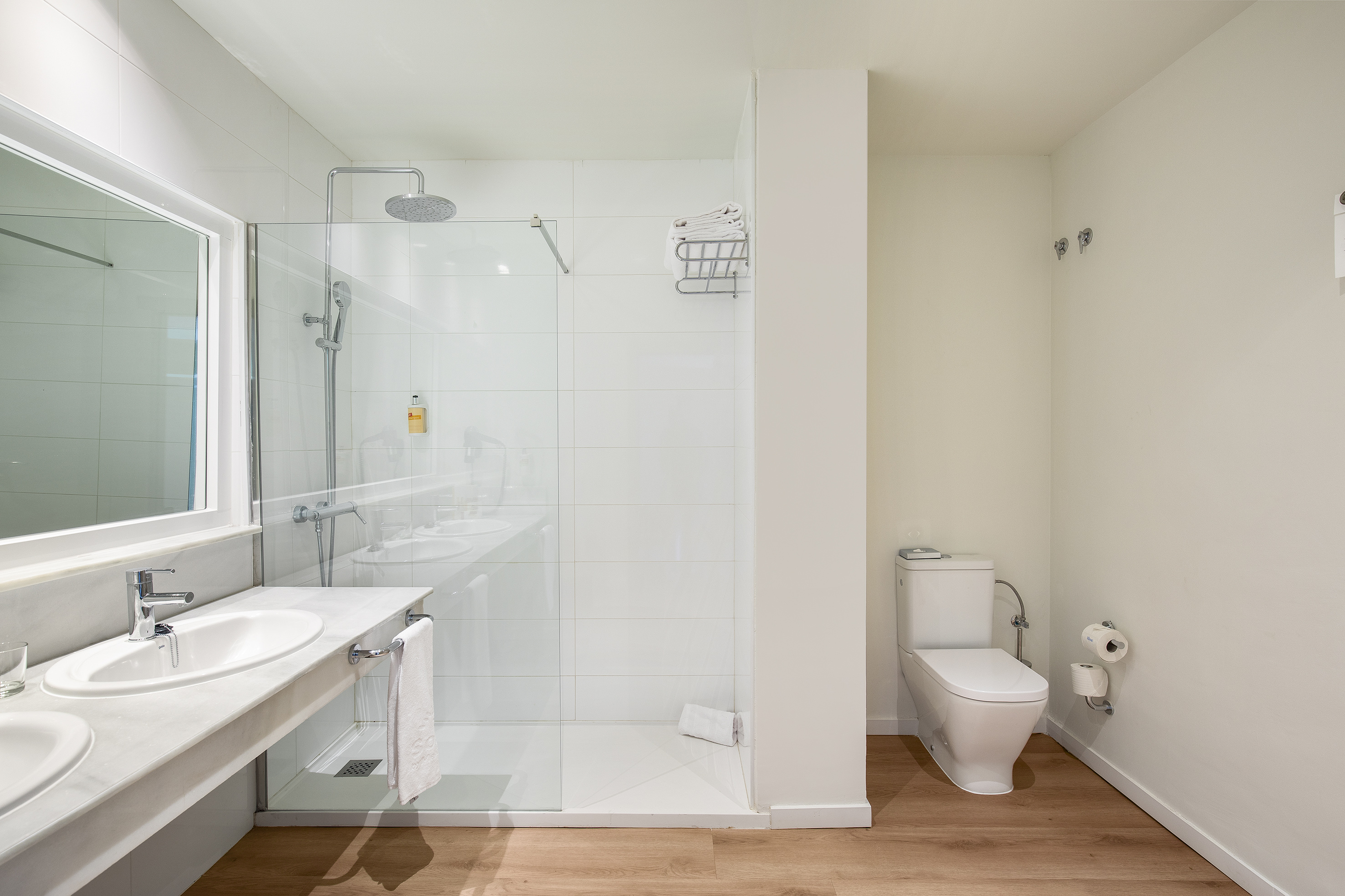 Bright hotel bathroom with walk-in shower, double vanity, and toilet.