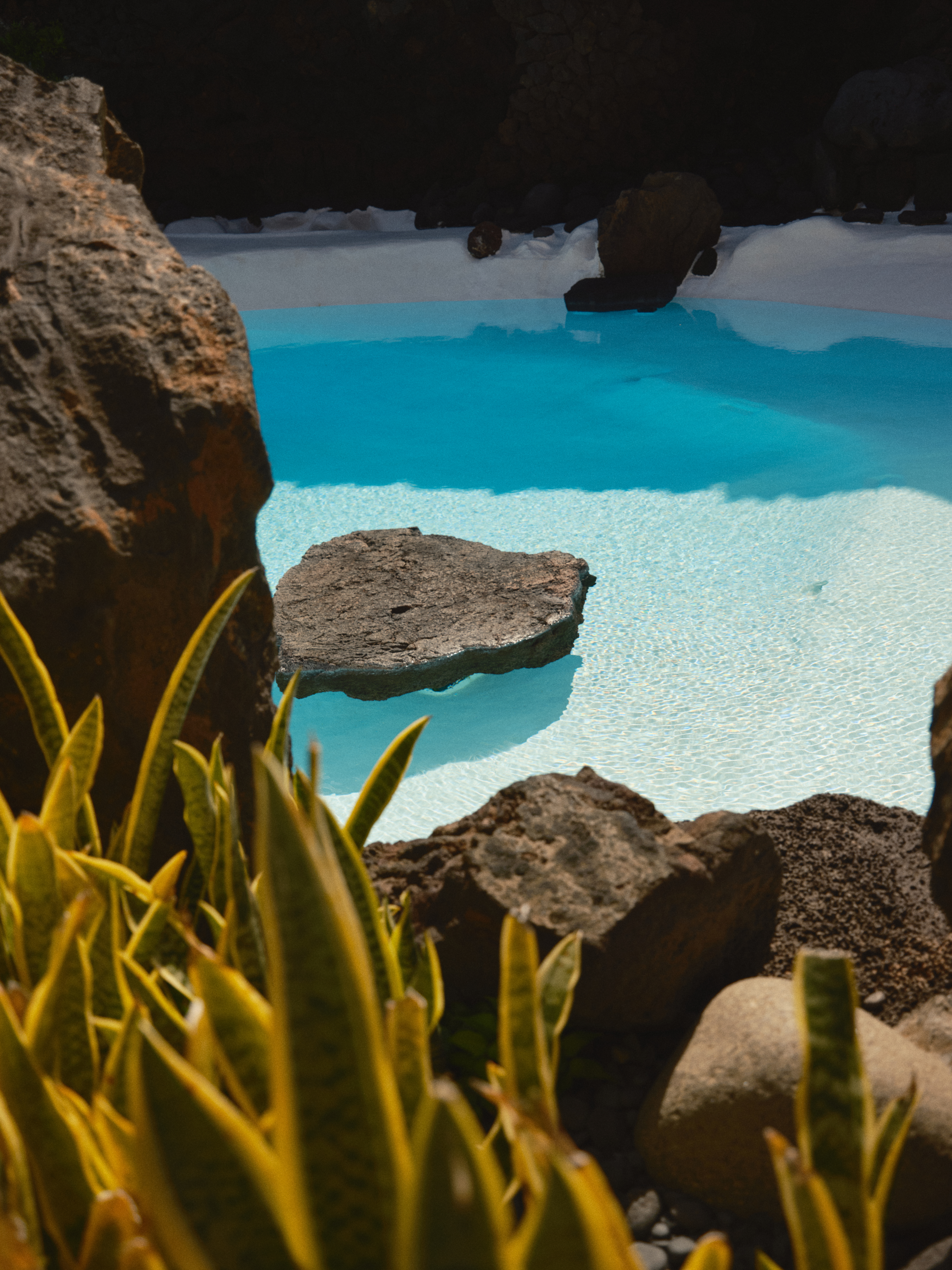 Natural blue pool with dark volcanic rocks and vivid tropical plants.