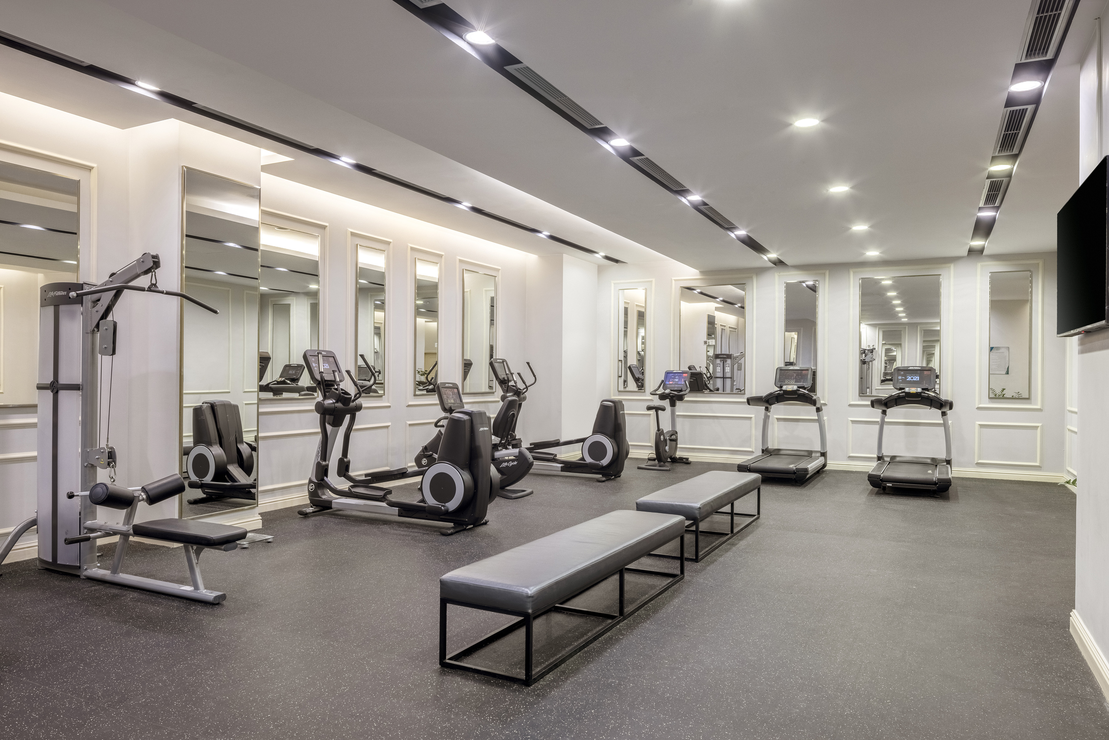 Modern gym with cardio and strength equipment, mirrored walls, and benches.