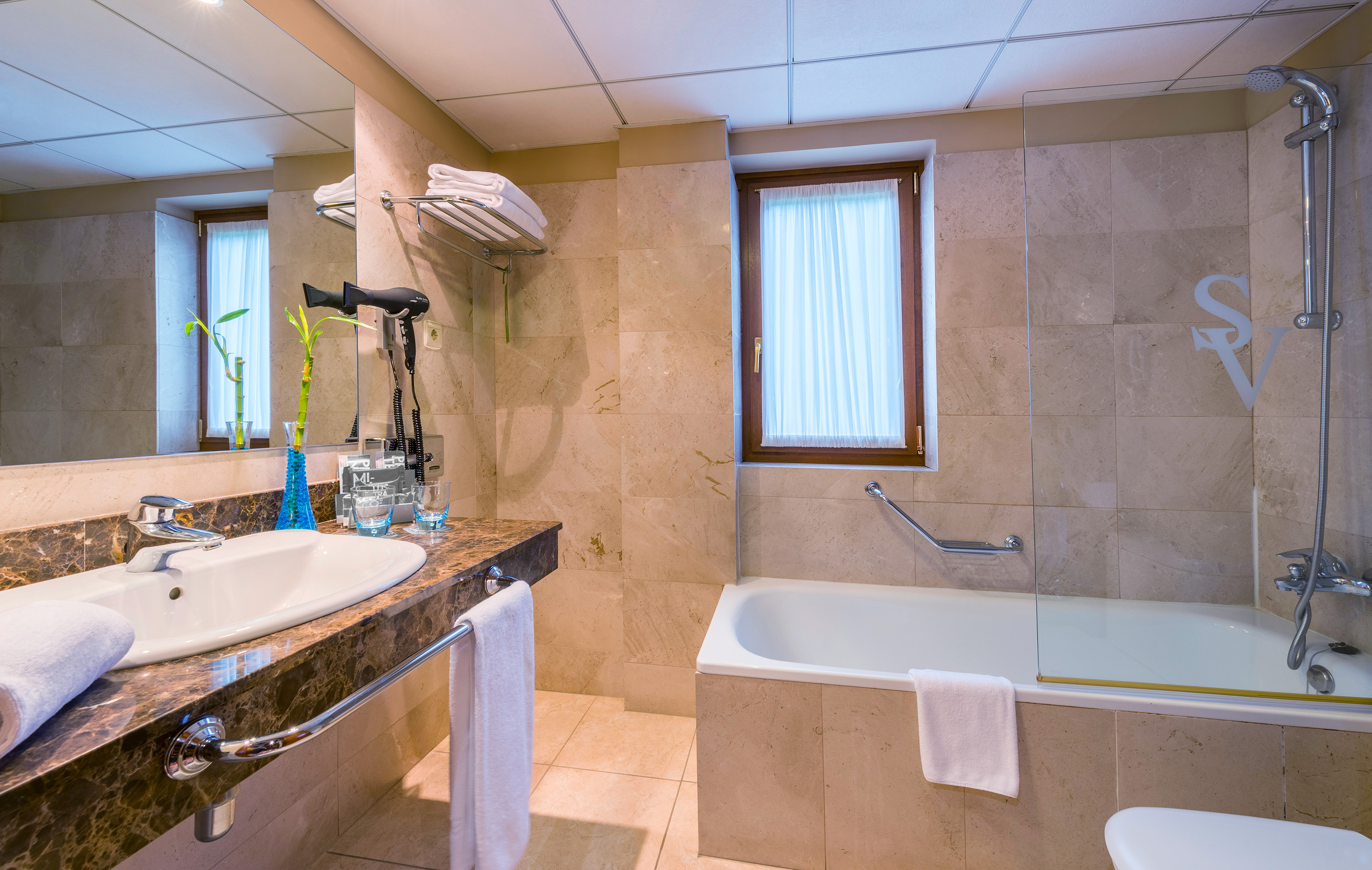 Modern hotel bathroom with marble vanity, sink, bathtub, and shower.