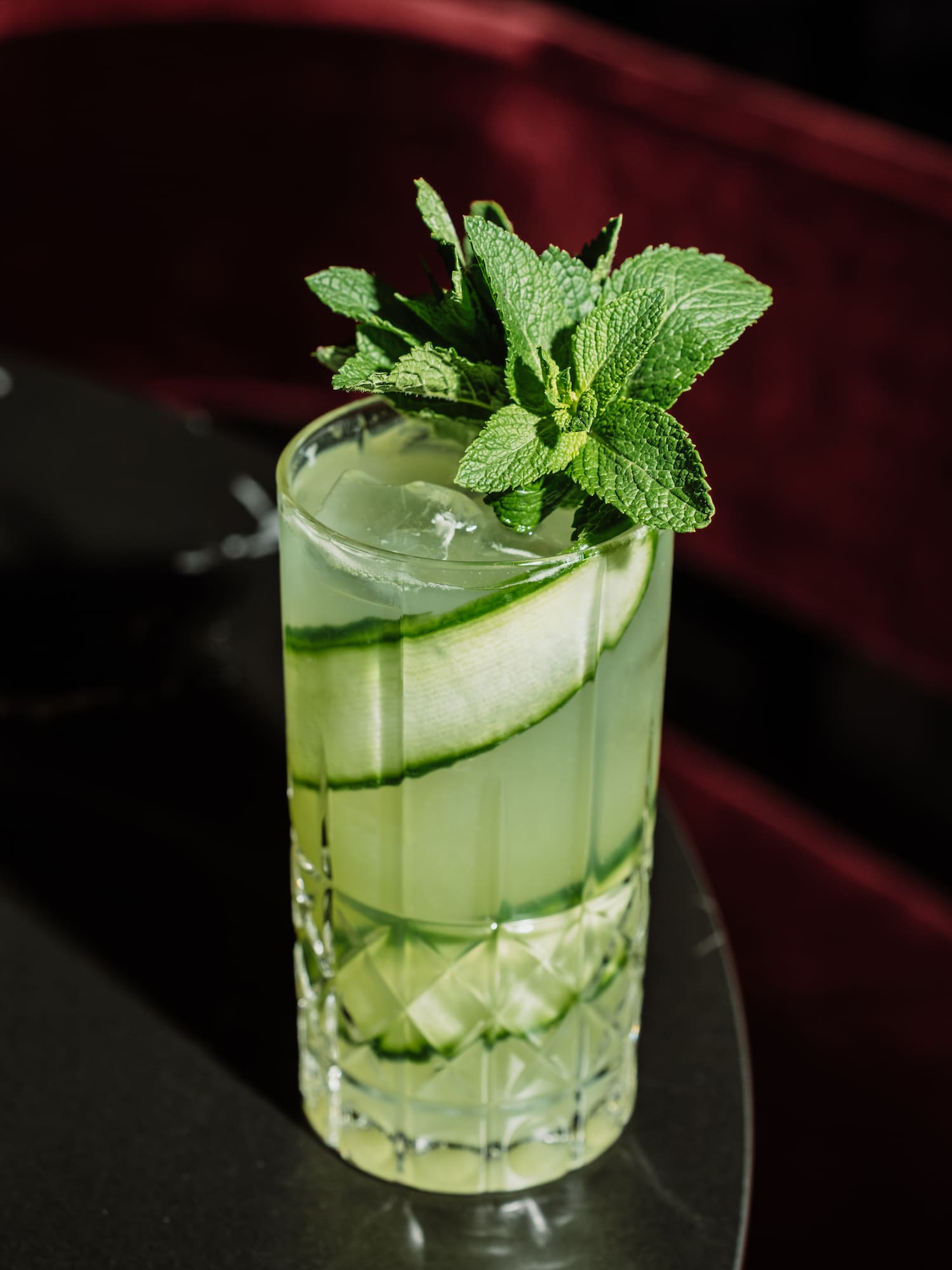 Cucumber mint cocktail with ice in a textured glass, bar setting.