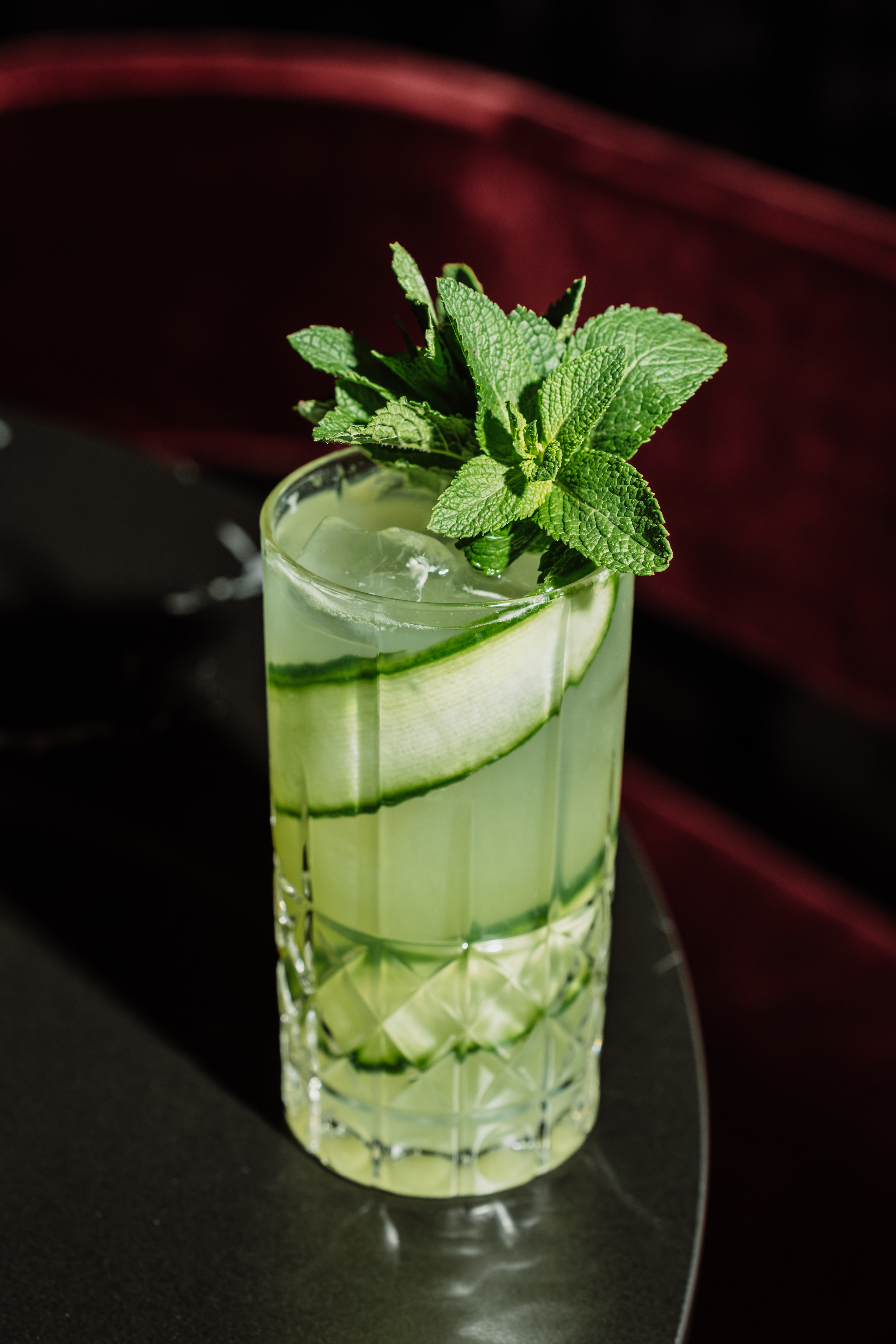Cucumber mint cocktail with ice in a textured glass, bar setting.