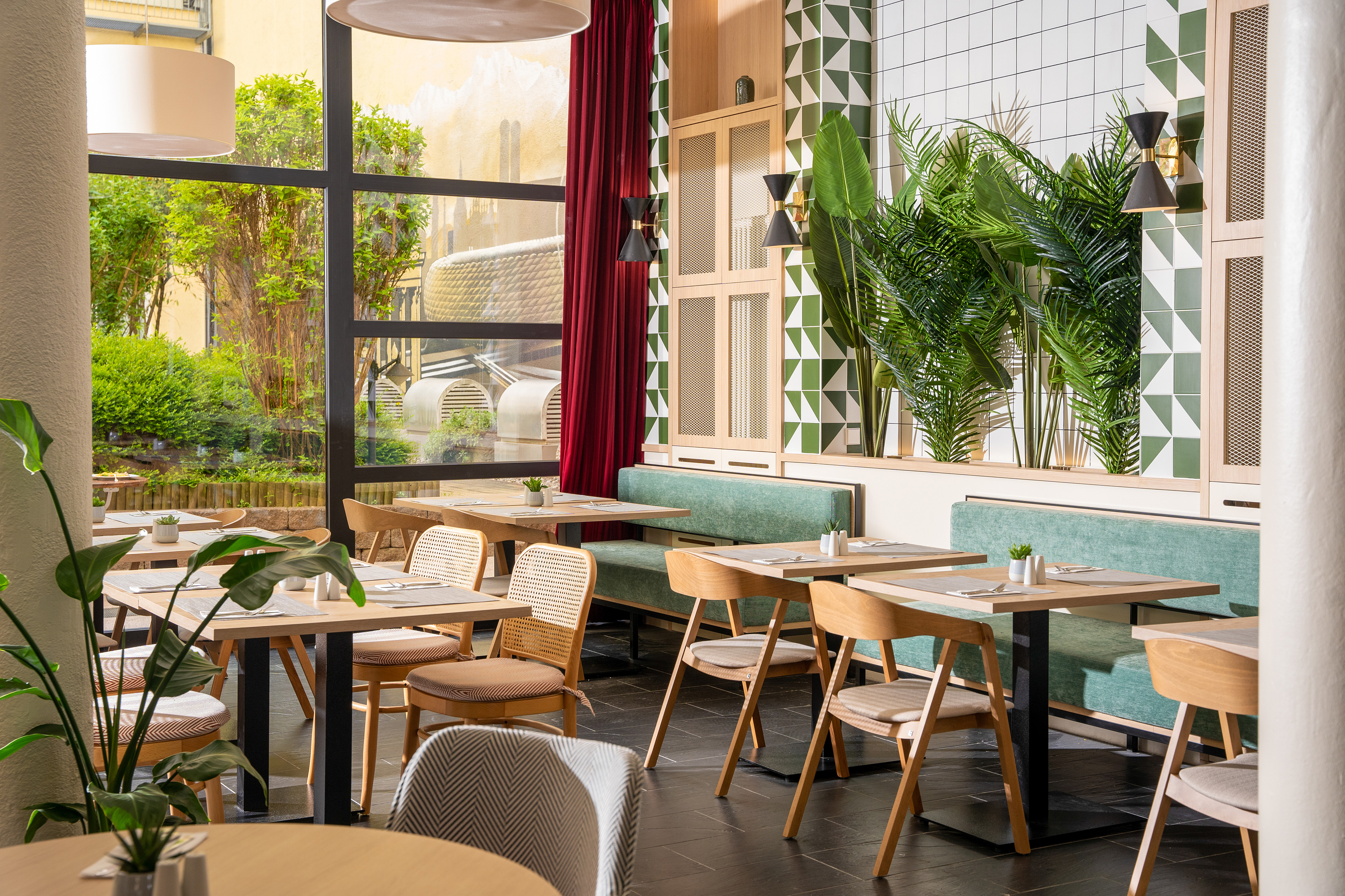Restaurant with green tiles, plants, wooden tables, and large windows.