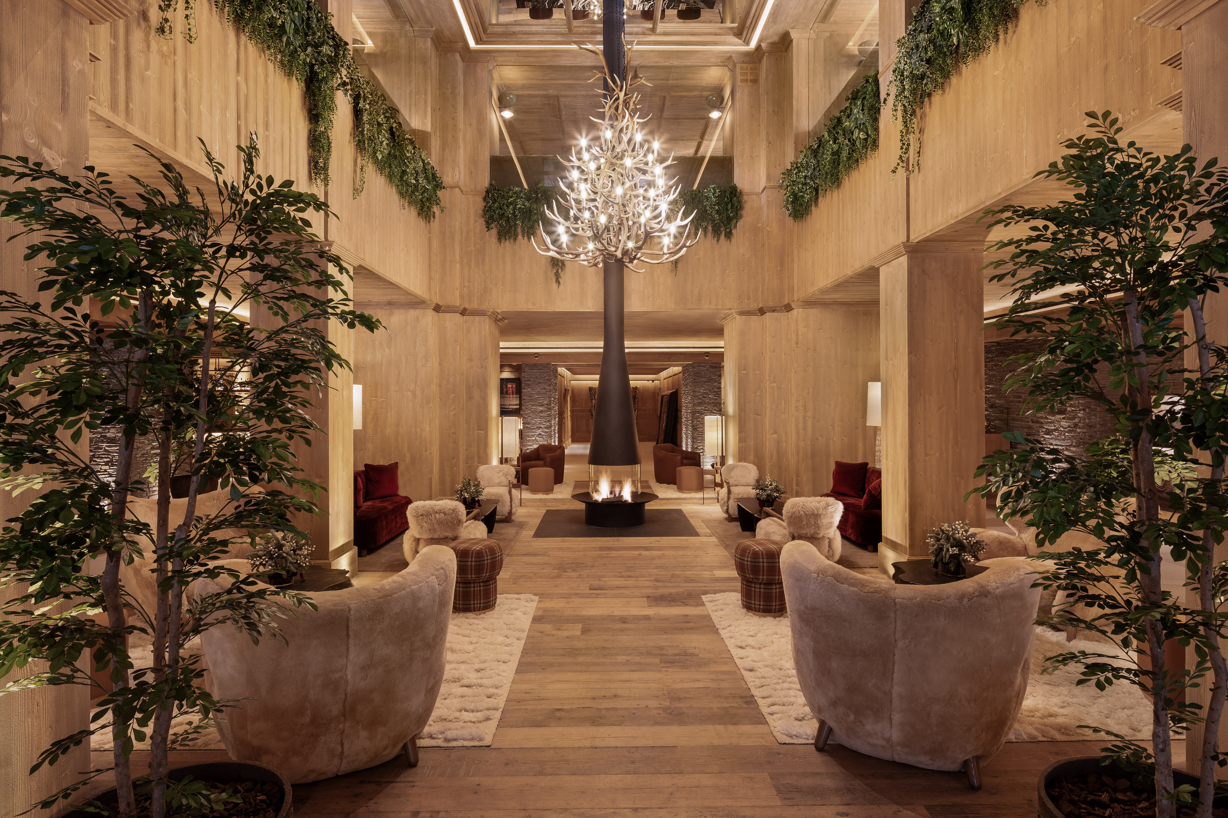 Inviting lodge lounge with central fireplace, antler chandelier, and warm wood interior.