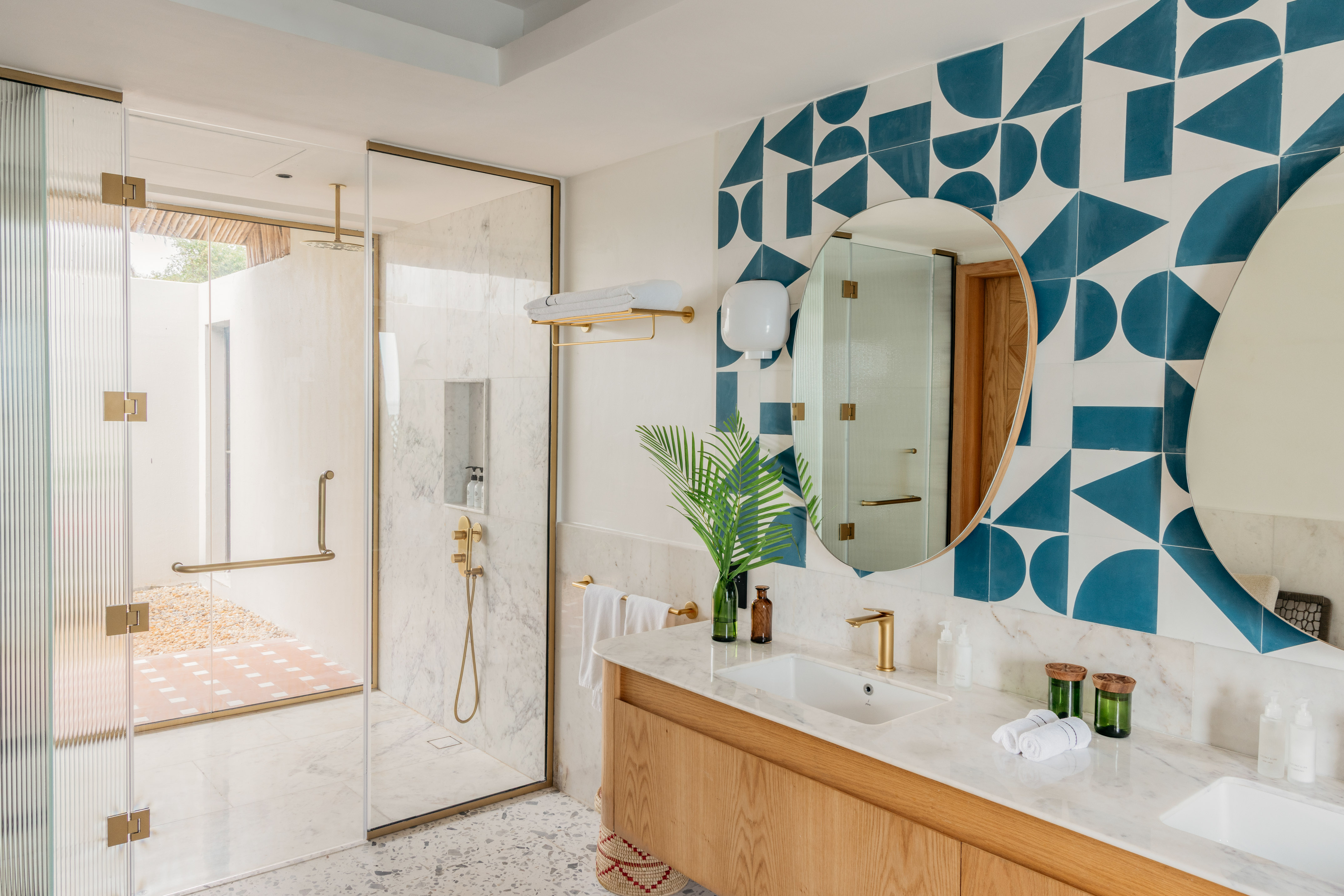 Luxury bathroom with glass shower, gold fixtures, and blue geometric tile wall.