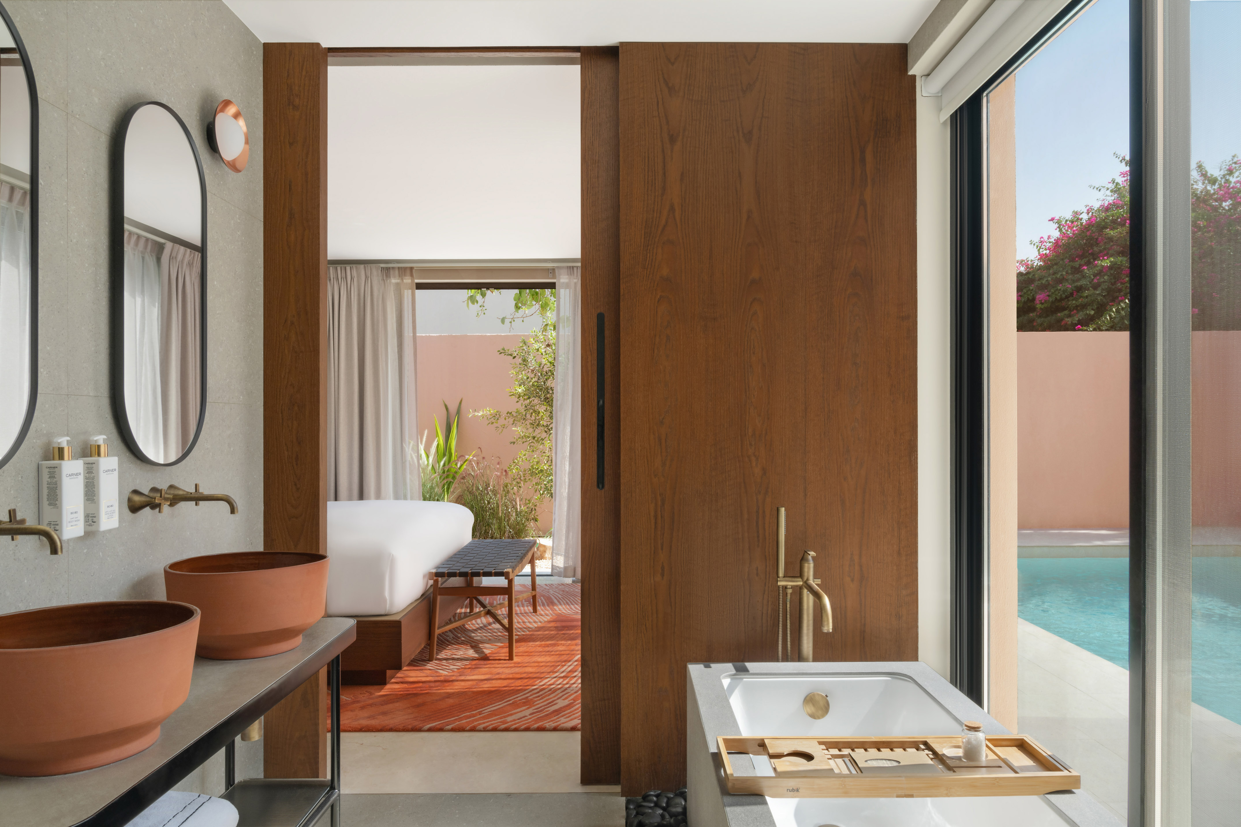 Bathroom with terracotta sinks, wood door to bedroom, and outdoor pool.