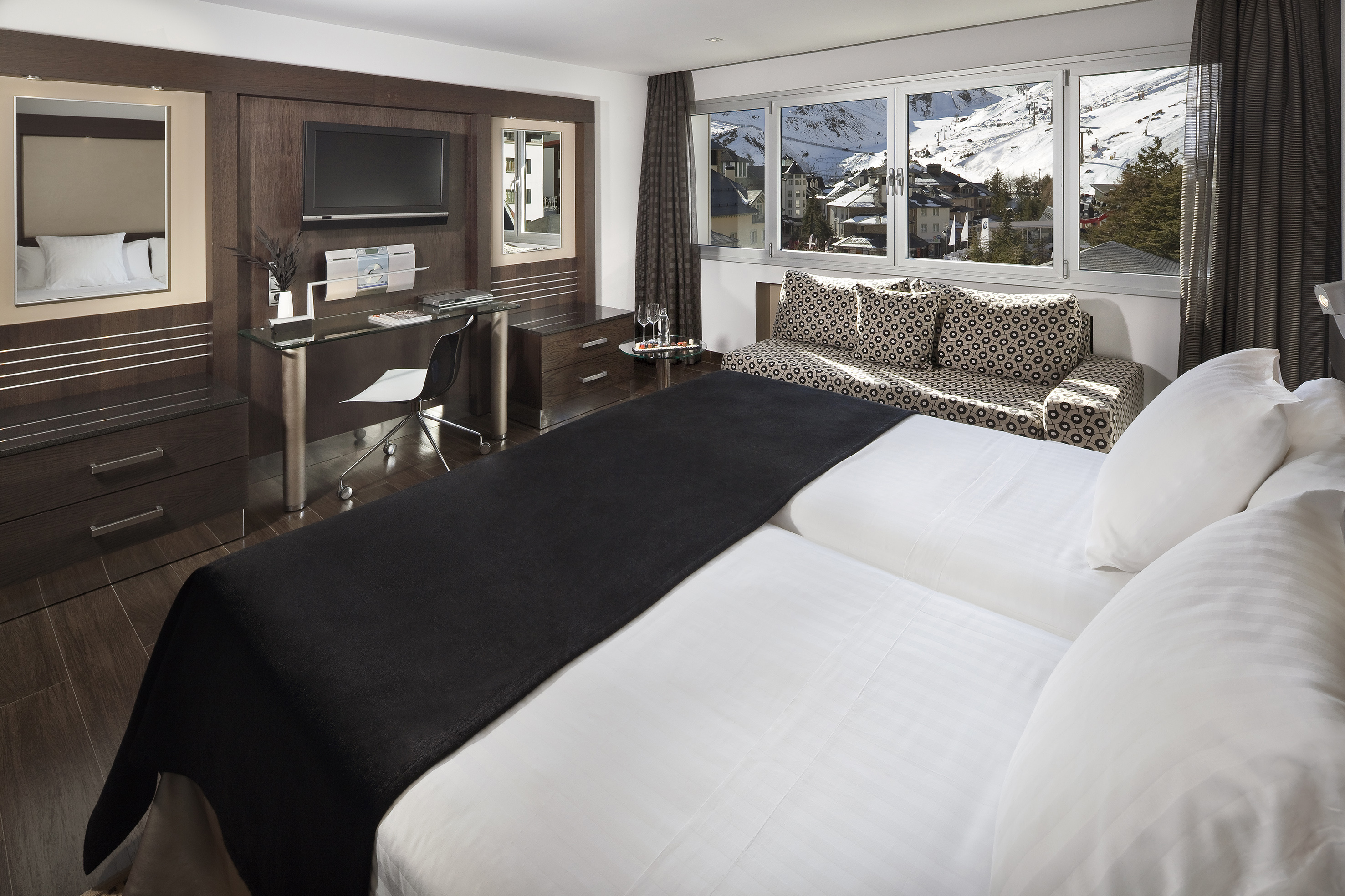 Stylish hotel bedroom with twin beds, desk, and scenic snowy mountain view.
