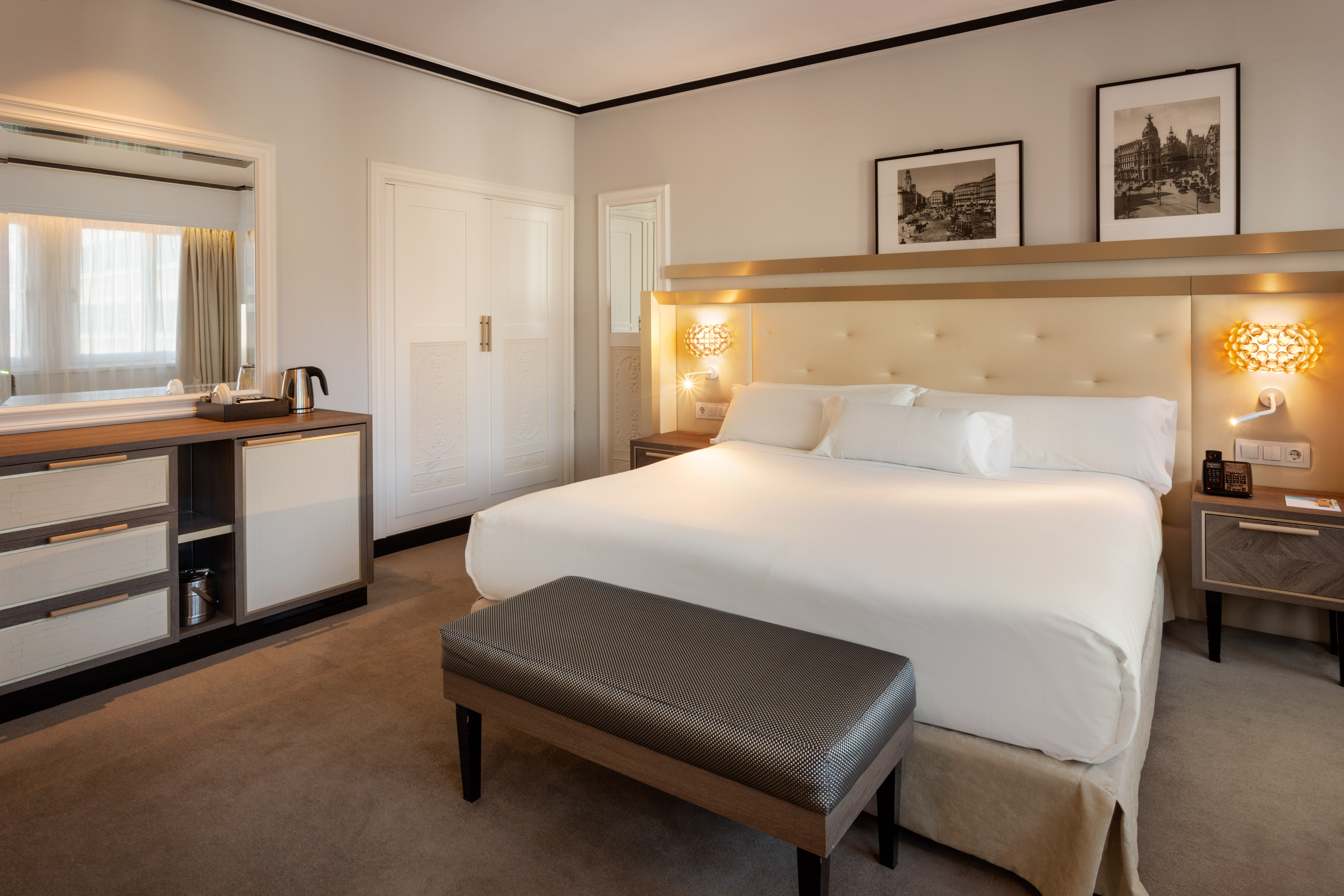 Modern hotel room with king bed, tufted headboard, cityscape art, and console.