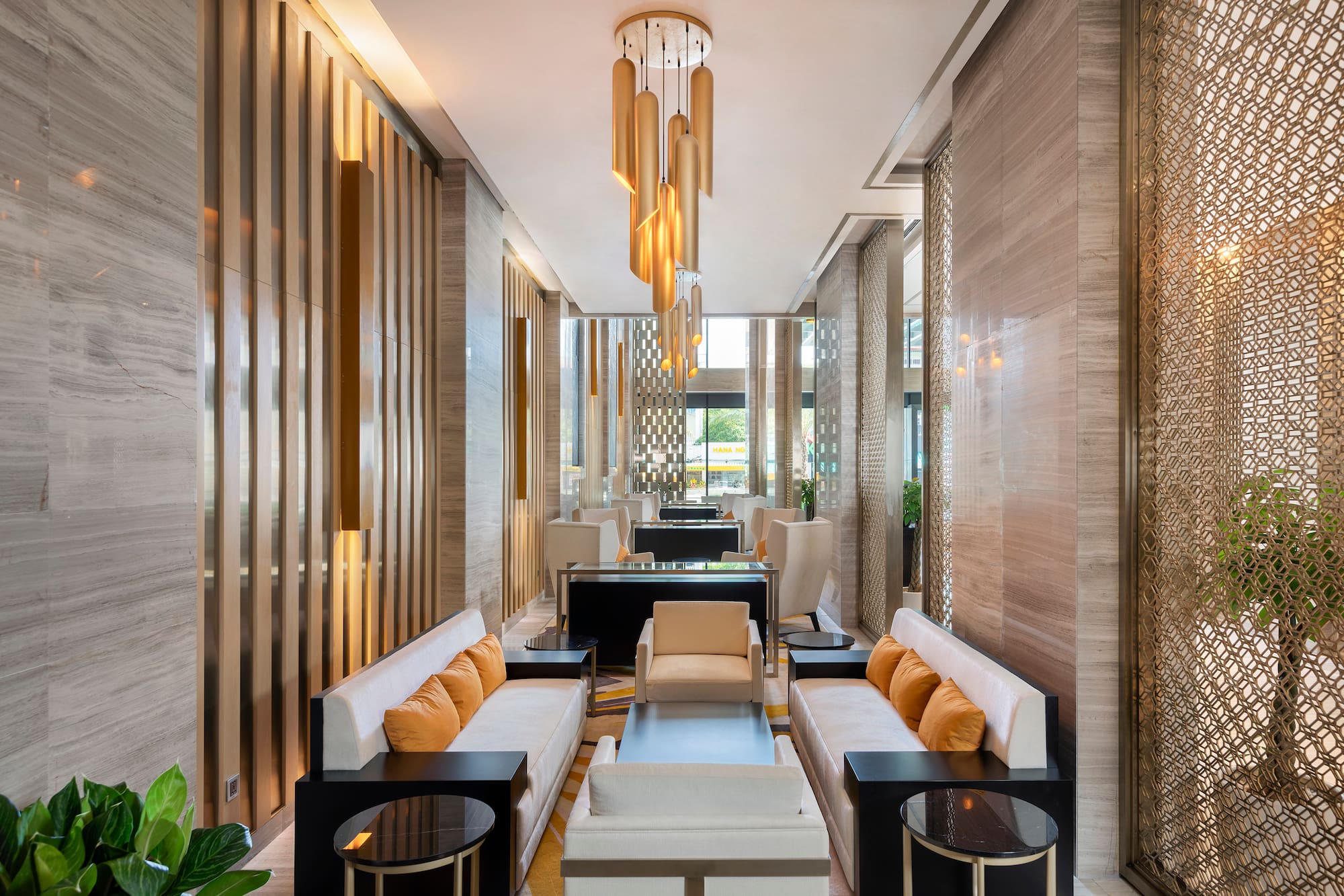 Spacious hotel lounge with modern gold chandelier, cream sofas, and marble walls.