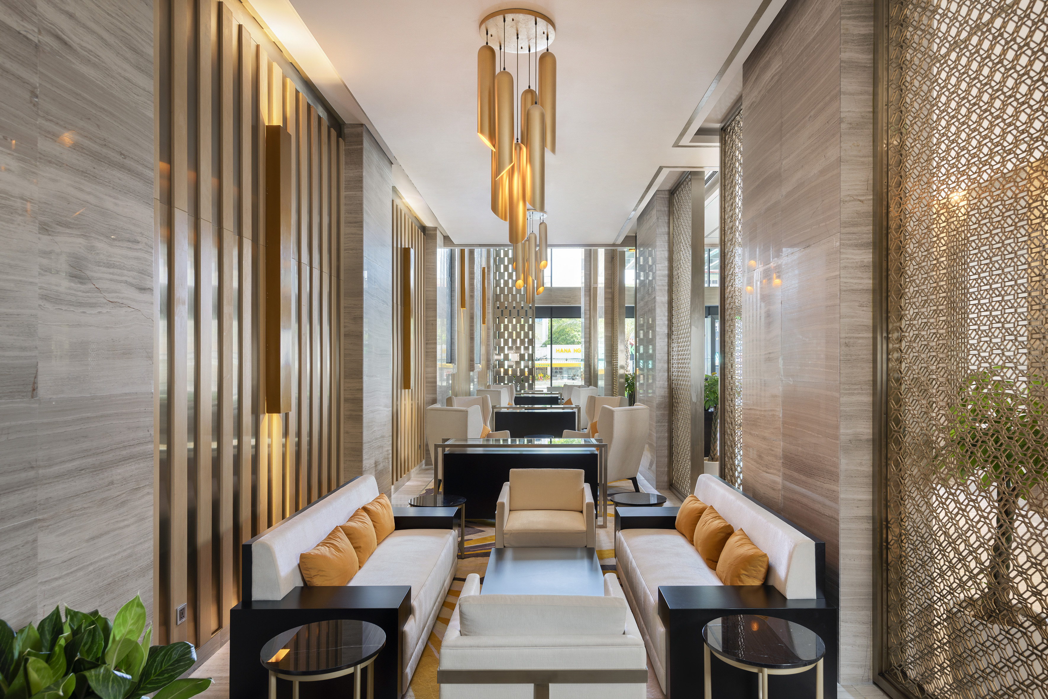 Spacious hotel lounge with modern gold chandelier, cream sofas, and marble walls.
