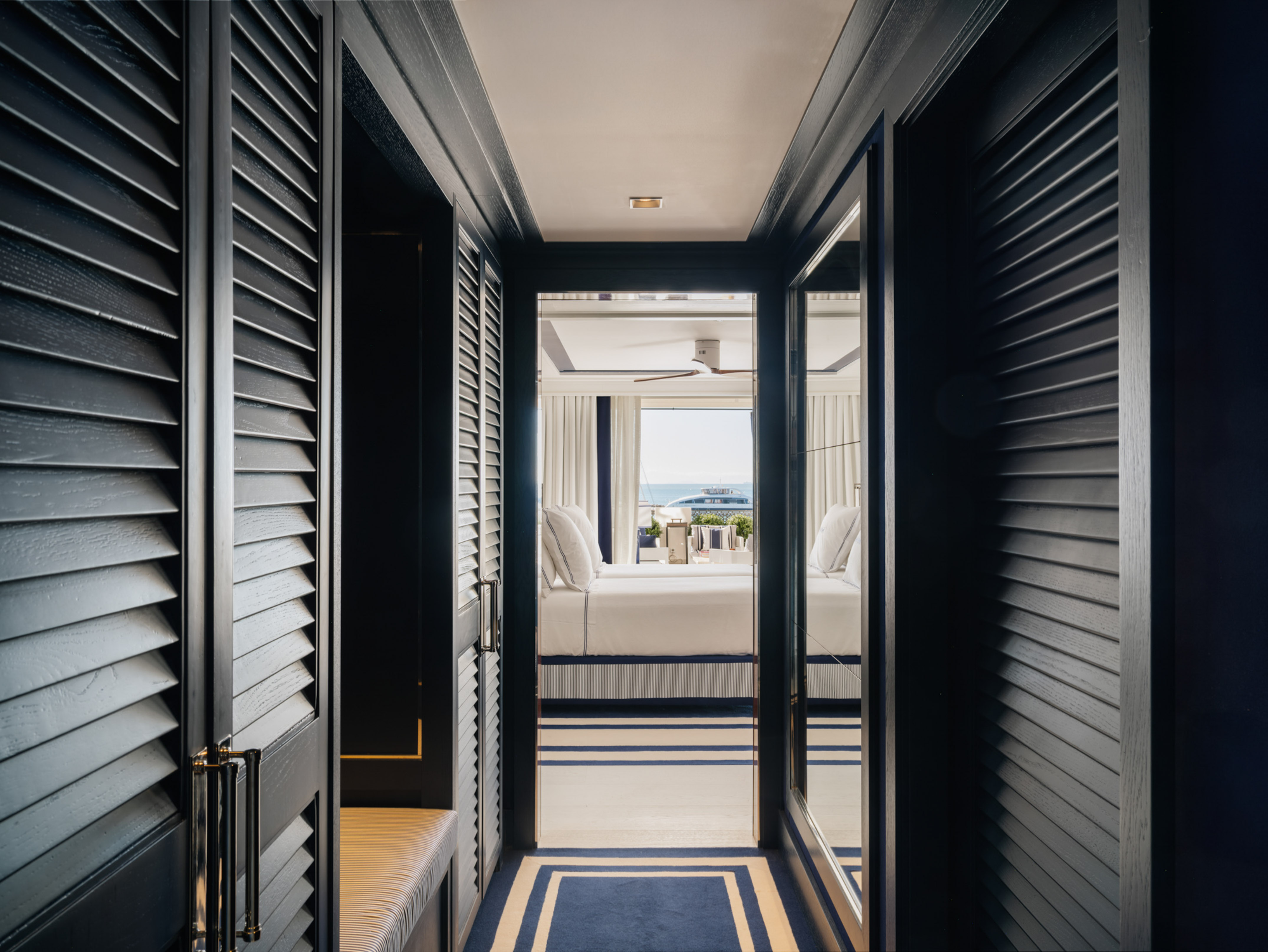 Nautical themed hallway leading to ocean view bedroom with dark wood louvers.