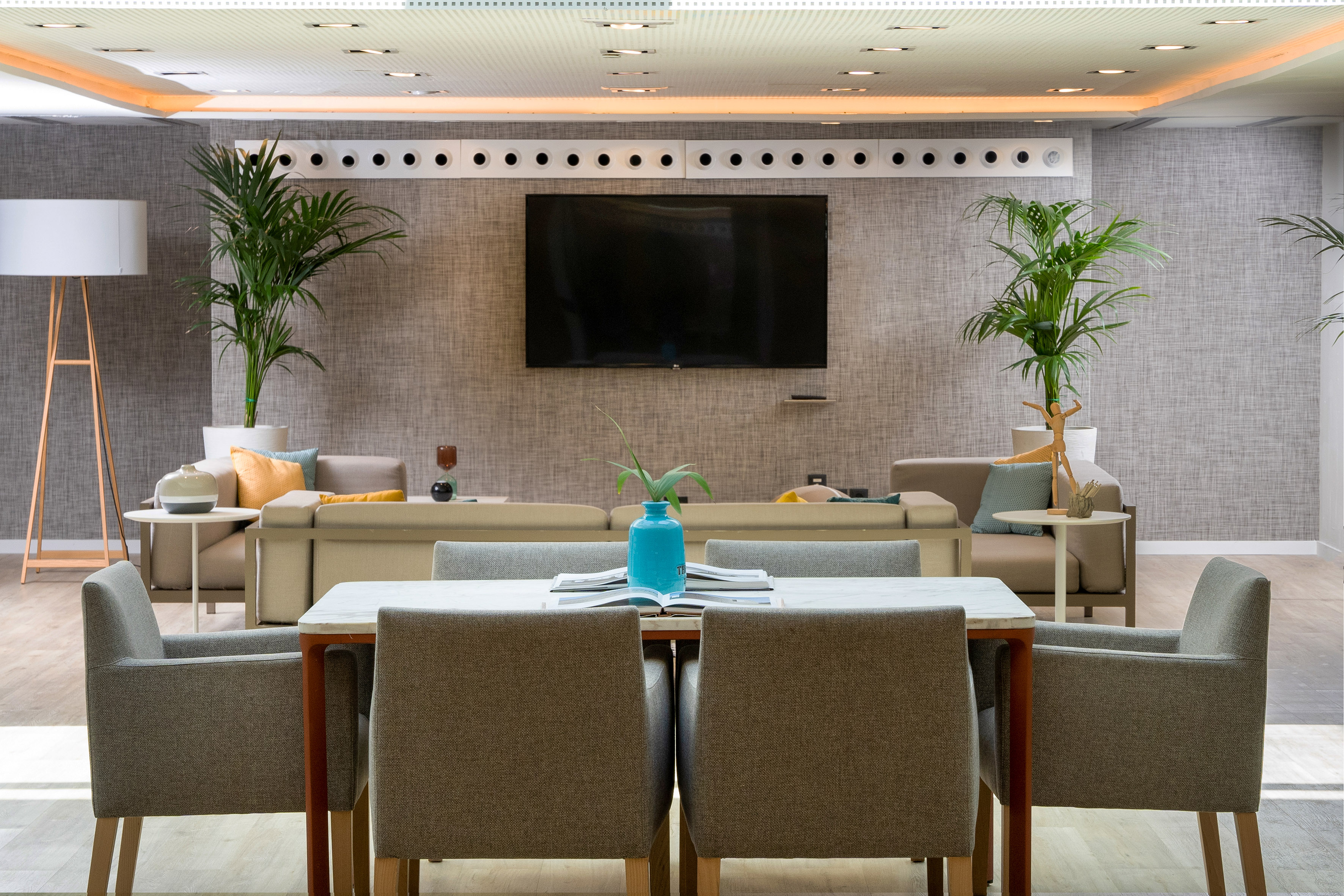 Modern lounge with dining table, sofas, wall TV, and potted plants.