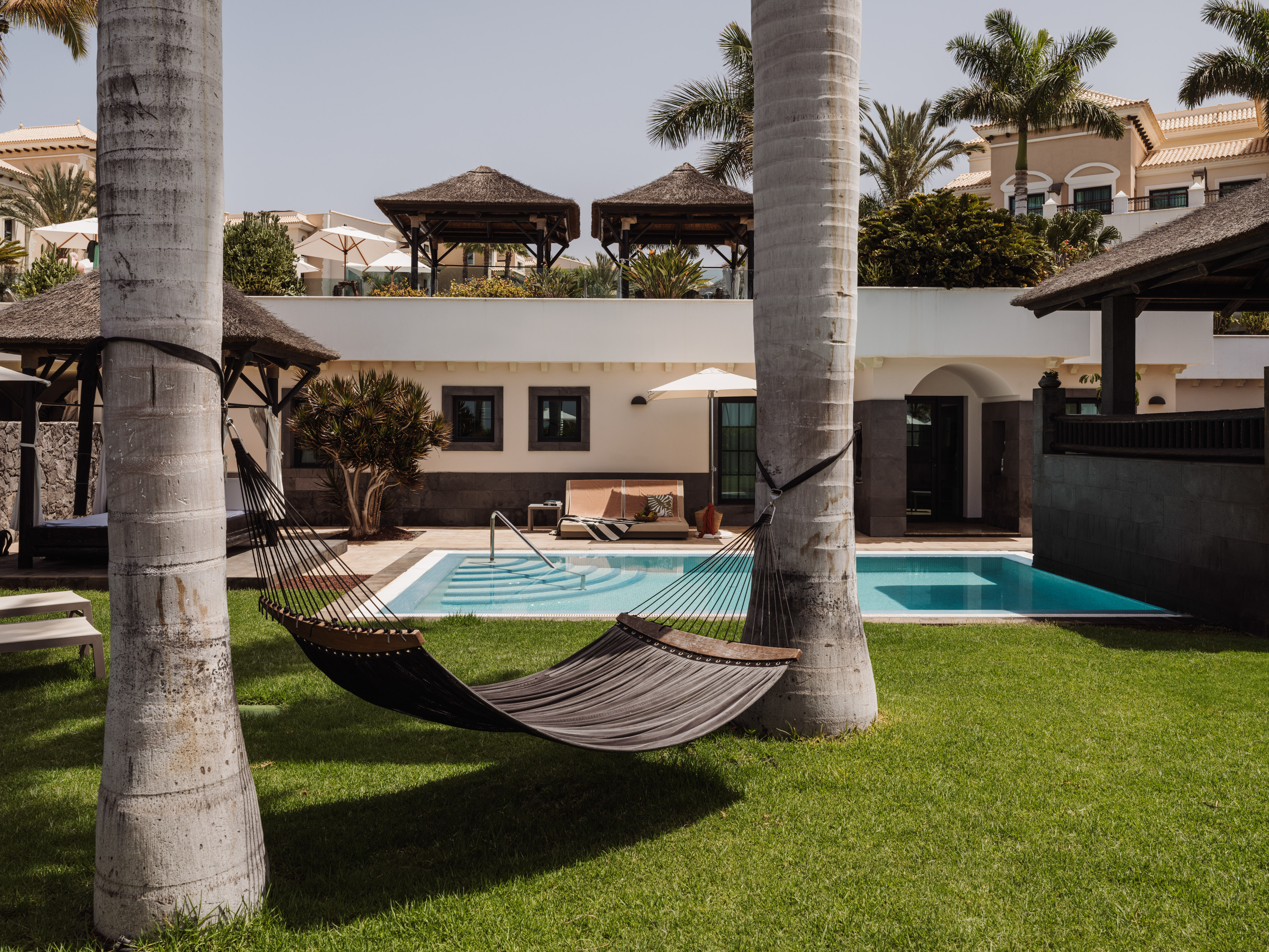 Hammock between palm trees by a swimming pool at a tropical resort.
