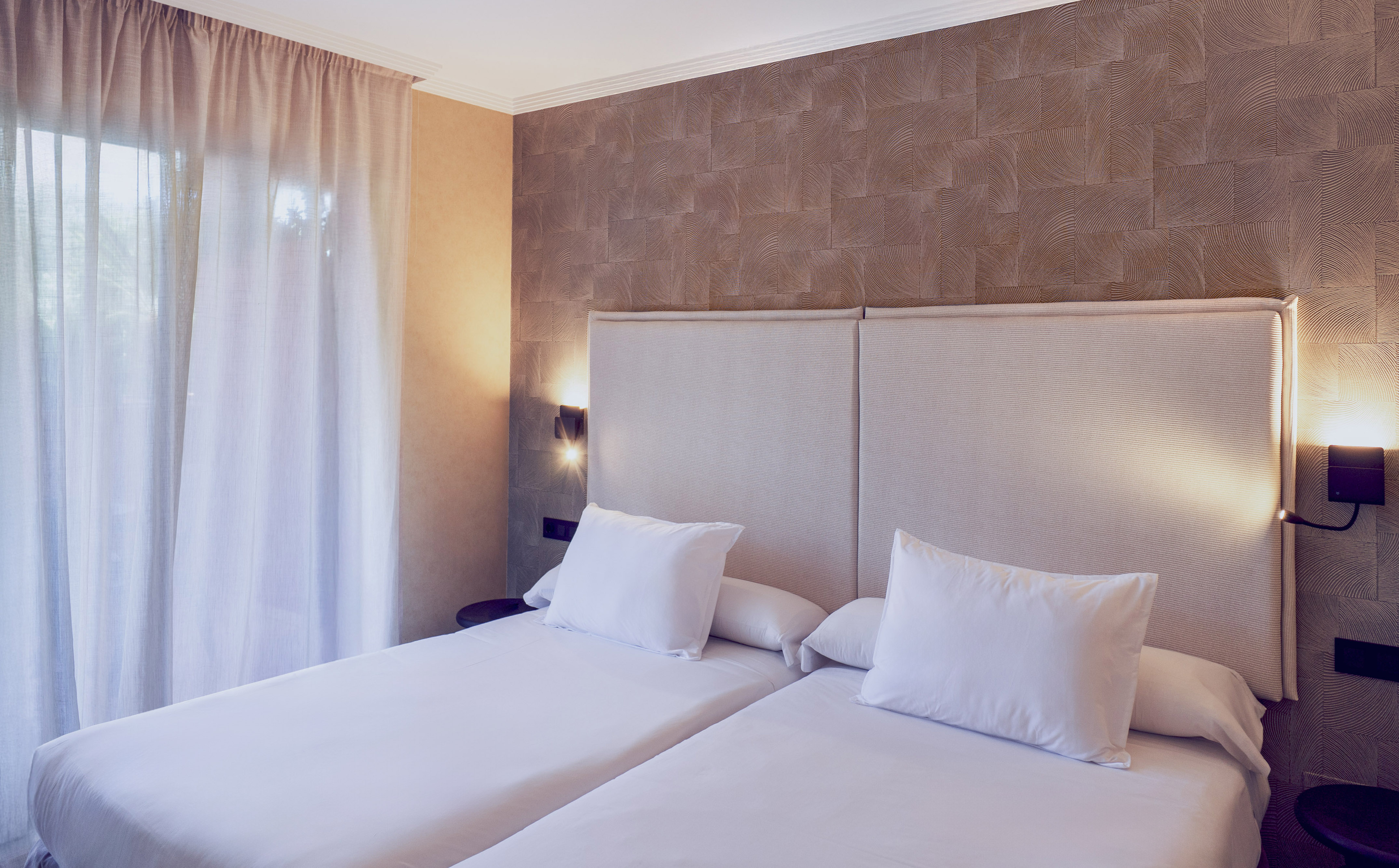 Modern hotel room with two twin beds, crisp white linens, and textured accent wall.