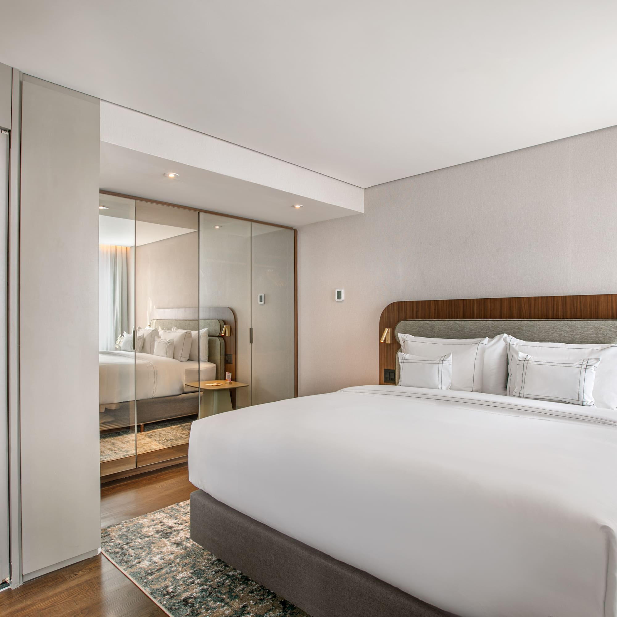 Modern hotel bedroom with king bed, reflective wardrobe, and ensuite vanity.
