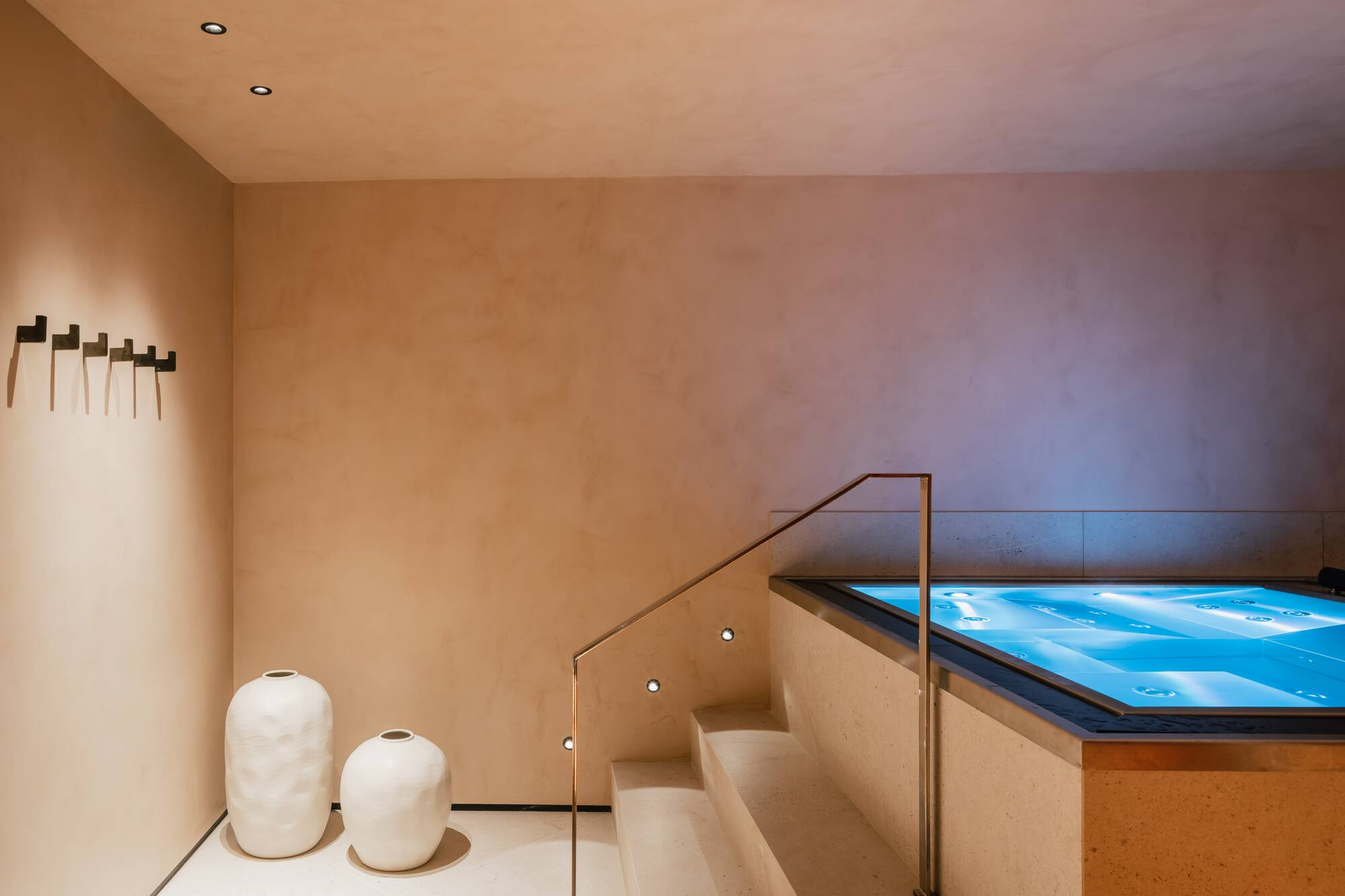 Diseño interior de spa de lujo con jacuzzi, escaleras y paredes beige.