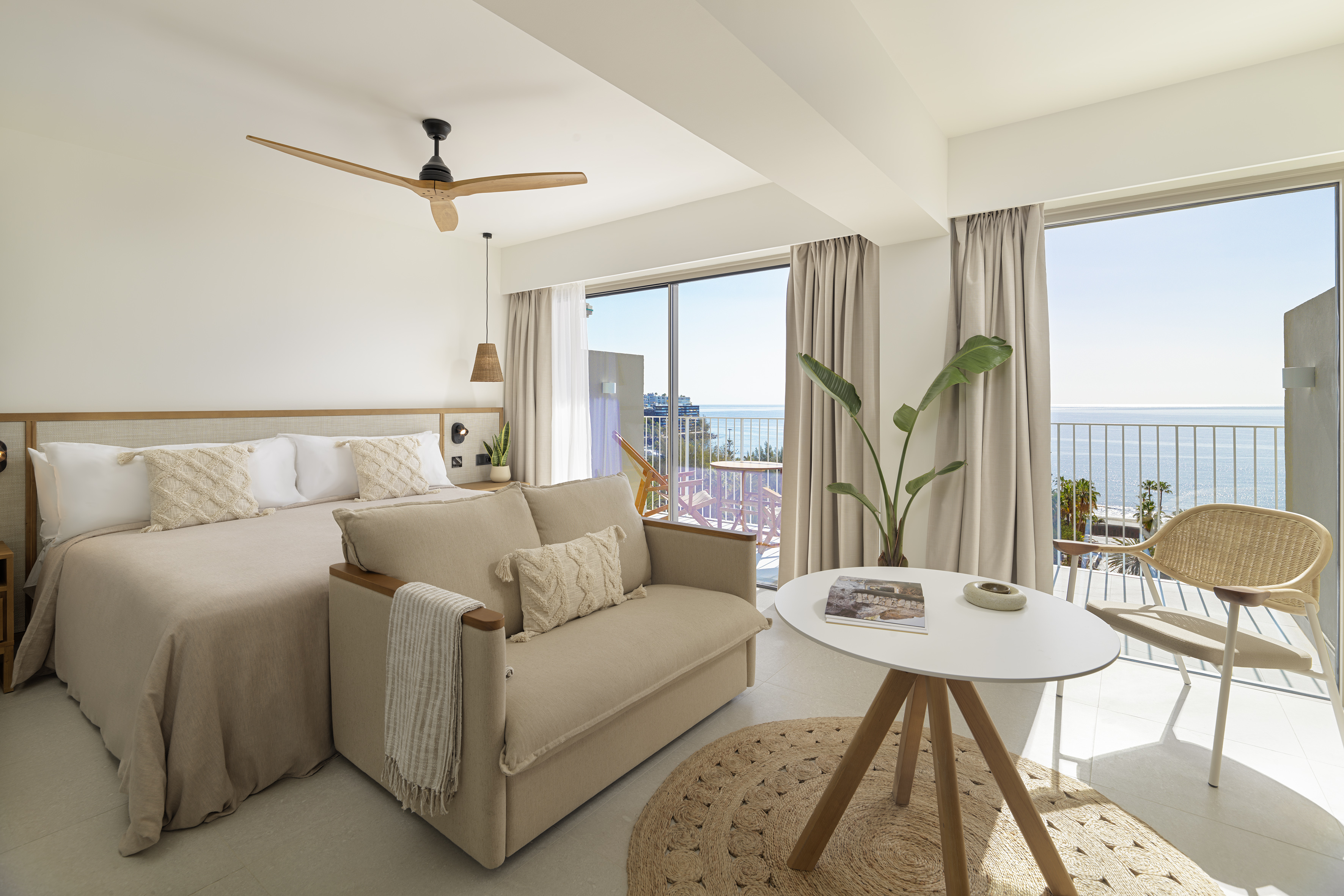 Modern ocean view hotel suite with bed, sofa, and balcony overlooking the sea.