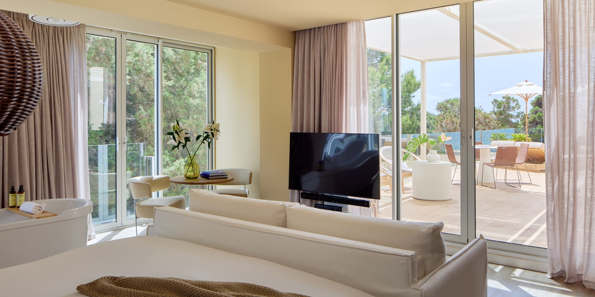 Luxury hotel suite bedroom with freestanding tub, TV, and private terrace view.