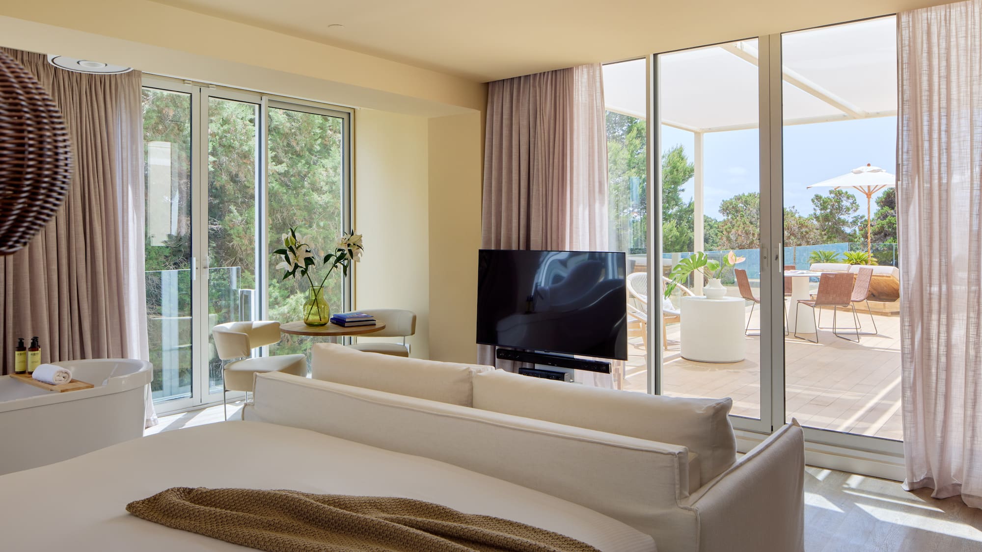 Luxury hotel suite bedroom with freestanding tub, TV, and private terrace view.