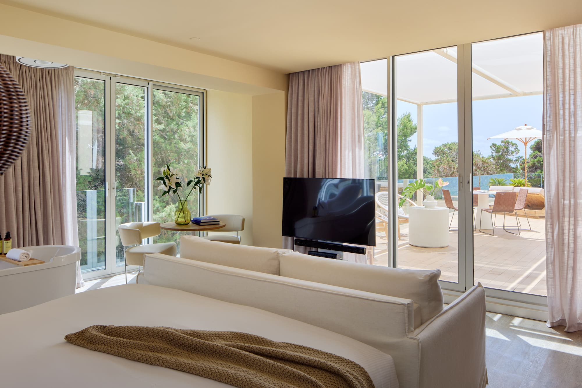 Luxury hotel suite bedroom with freestanding tub, TV, and private terrace view.
