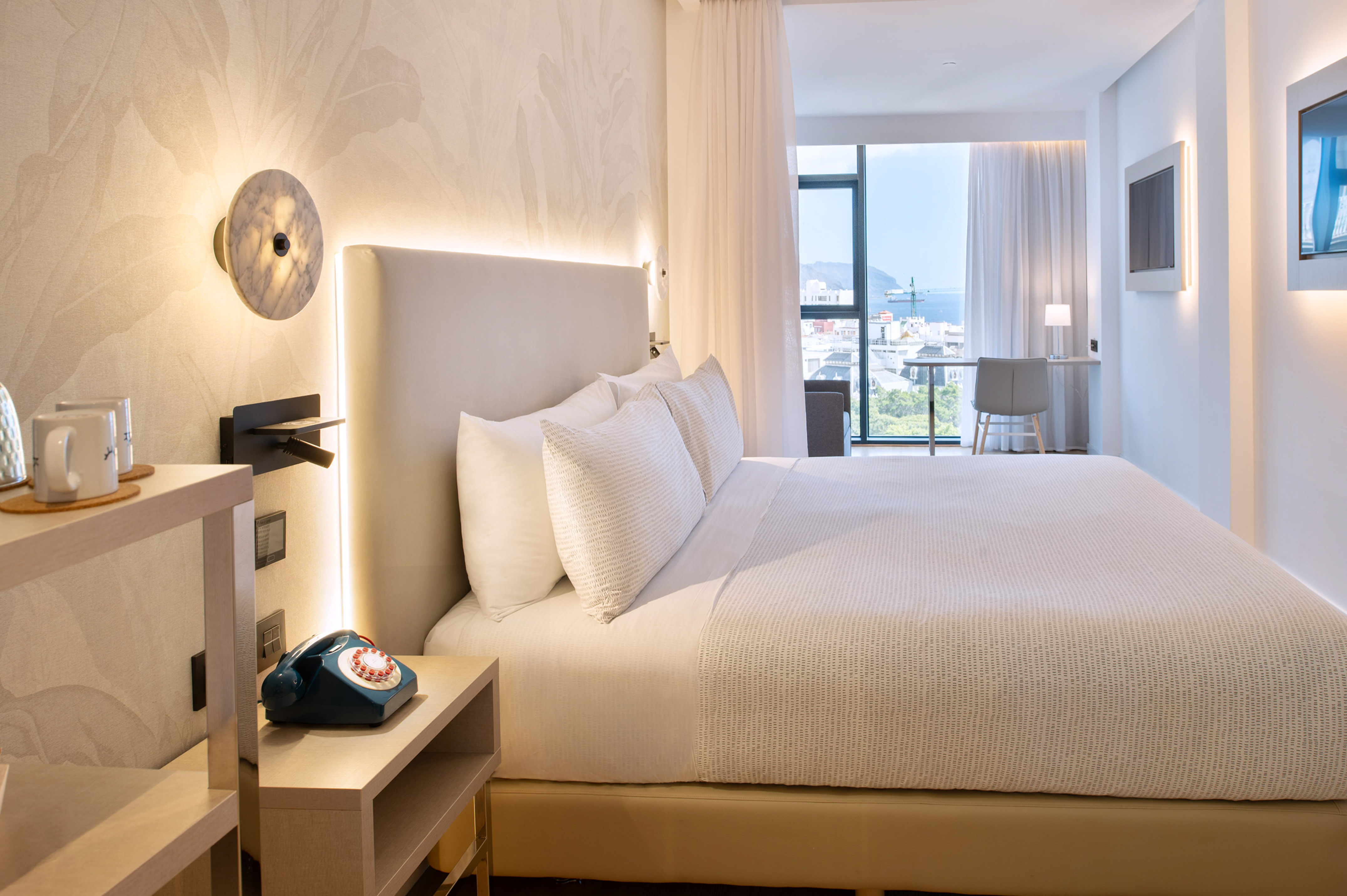Luxury hotel bedroom with king bed, marble sconce, and urban harbor view.