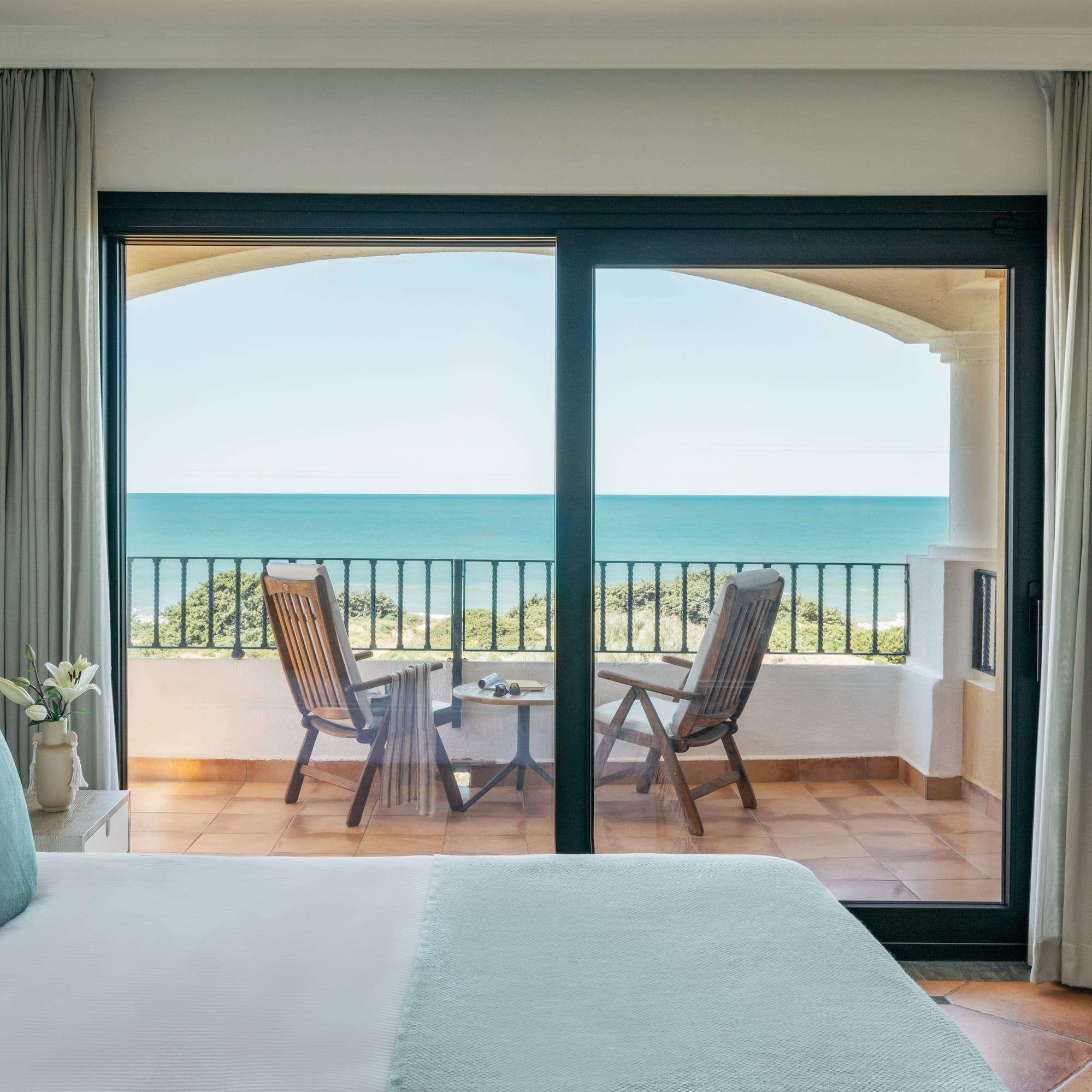 Hotel bedroom with ocean view balcony, chairs, and blue sea.