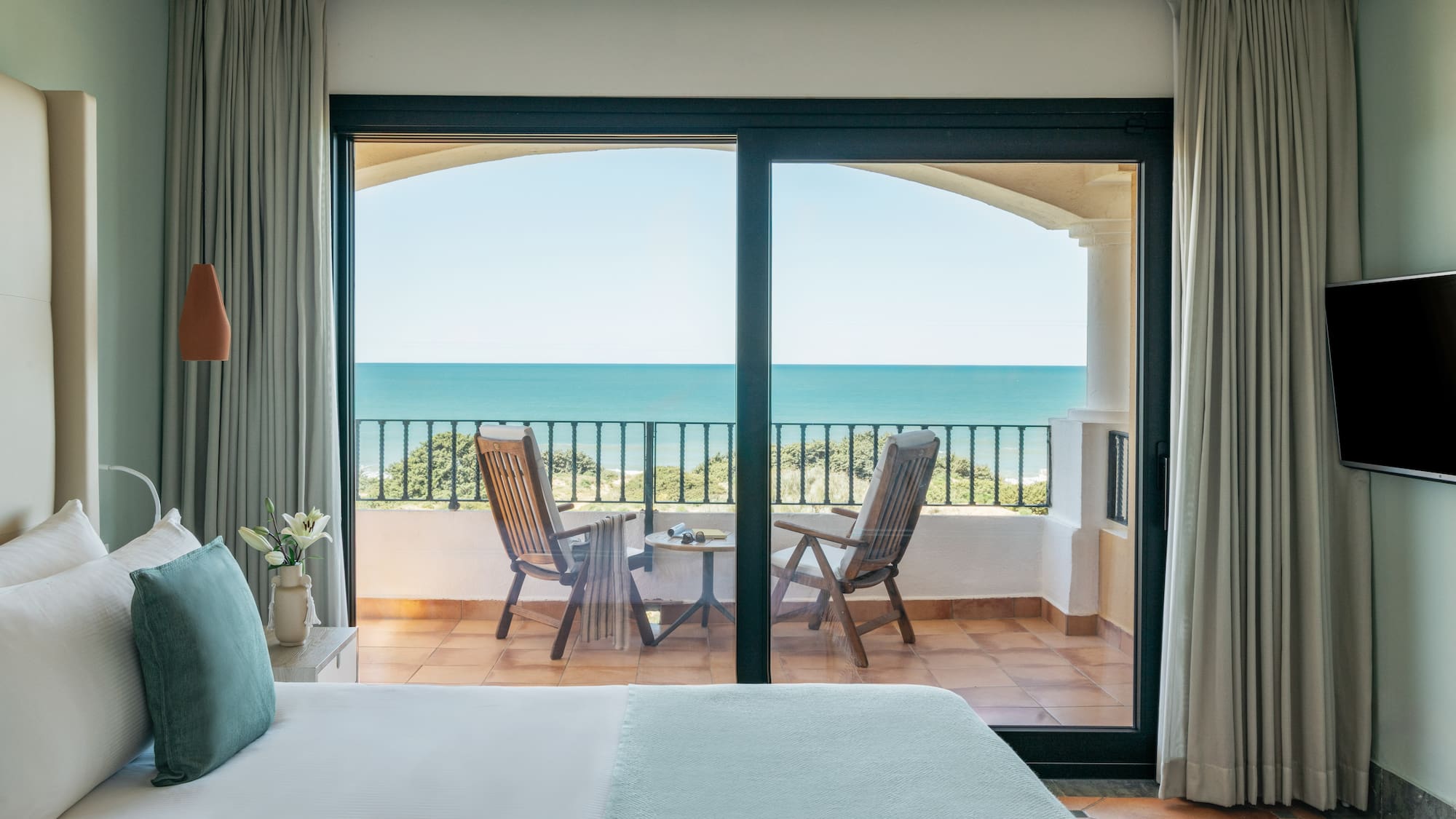 Hotel bedroom with ocean view balcony, chairs, and blue sea.