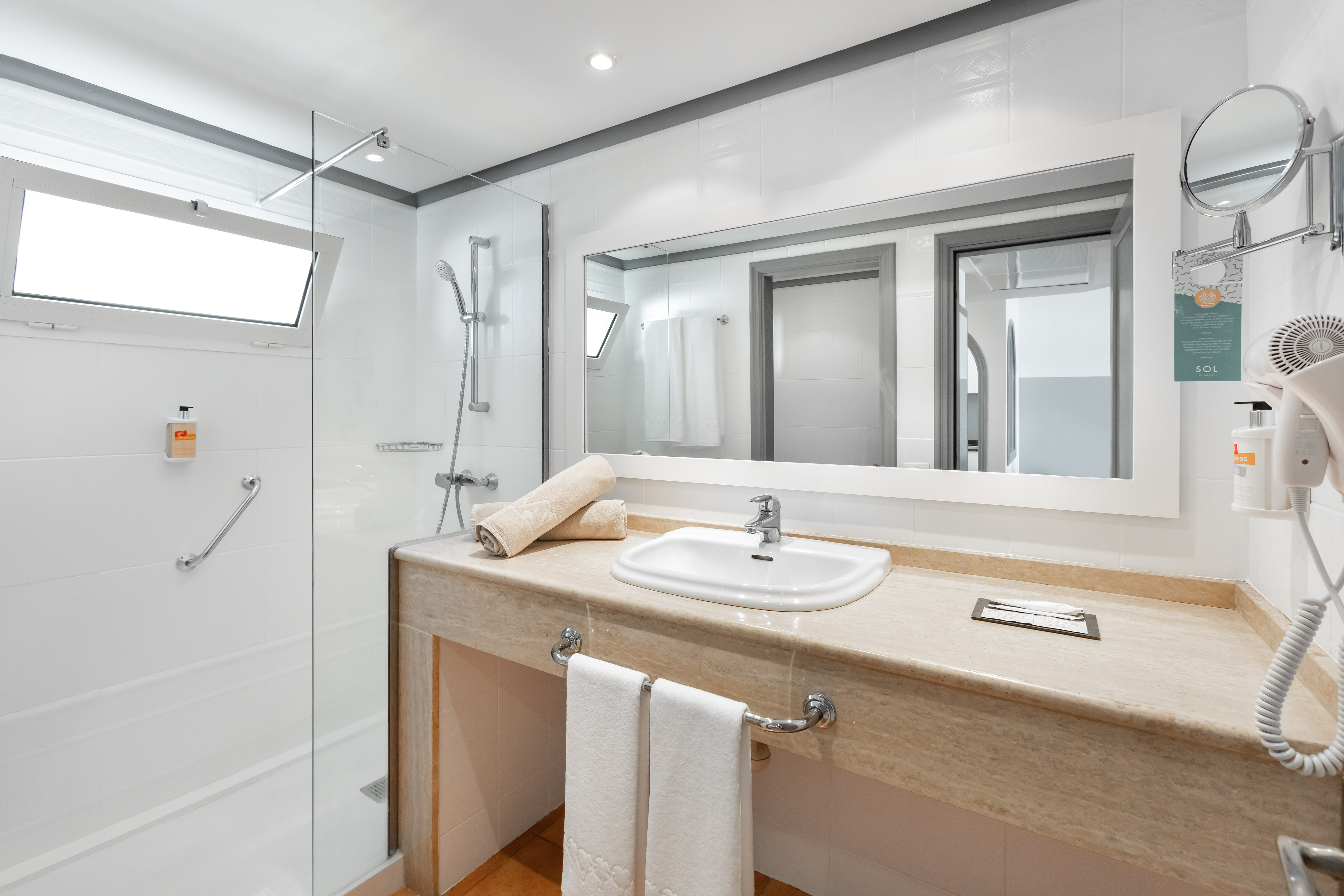 Bright modern hotel bathroom with walk-in shower, vanity, and large mirror.