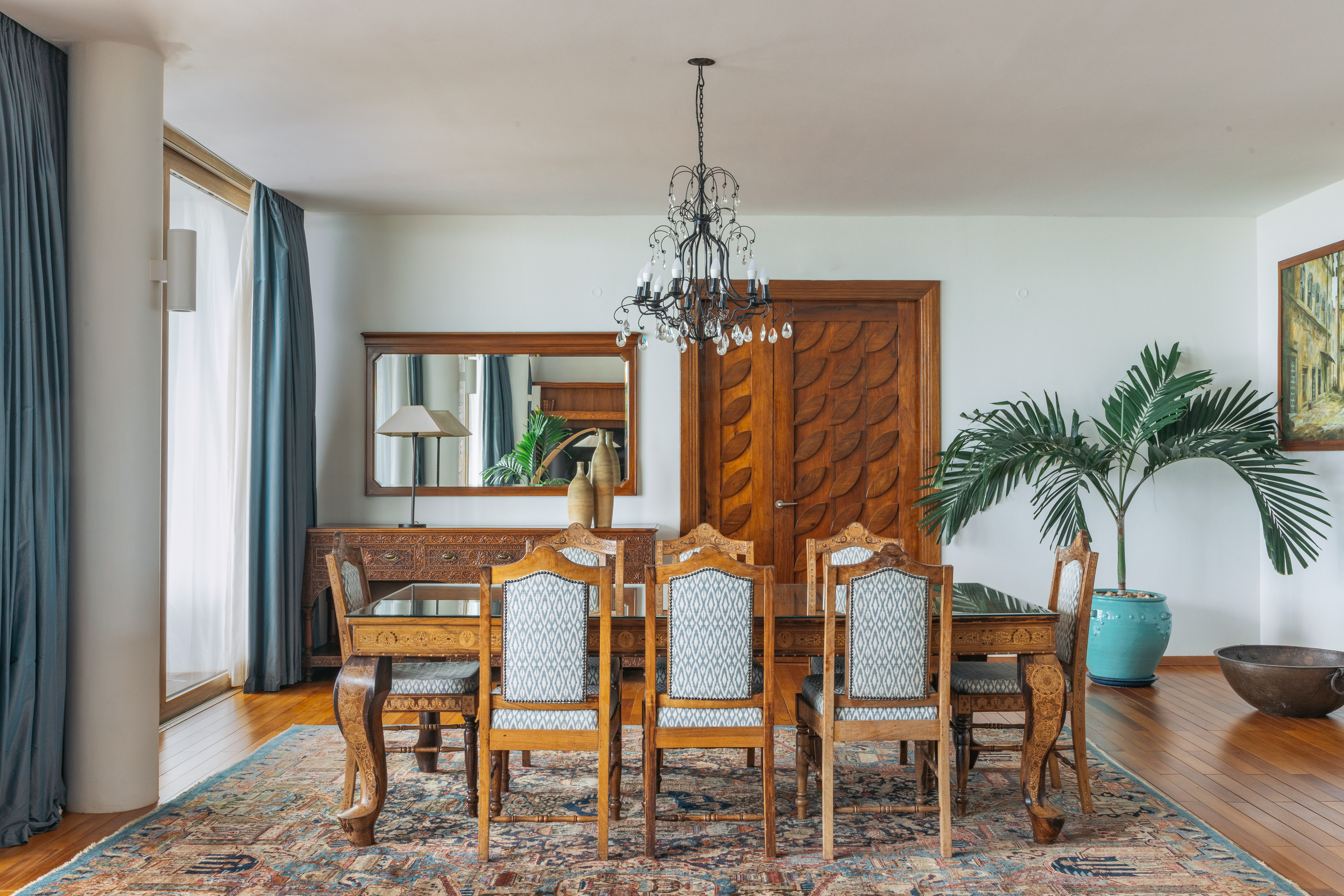 Elegant dining room with carved wooden table, patterned chairs, chandelier, and rug.