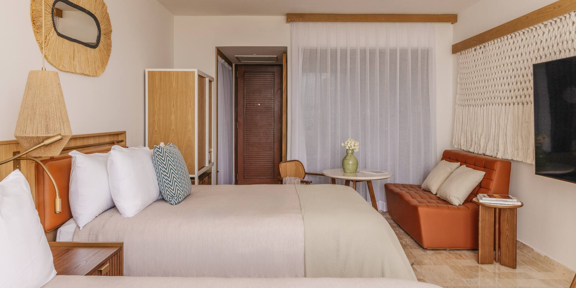 Tropical resort room with two beds, rattan mirror, orange sofa, and woven decor.