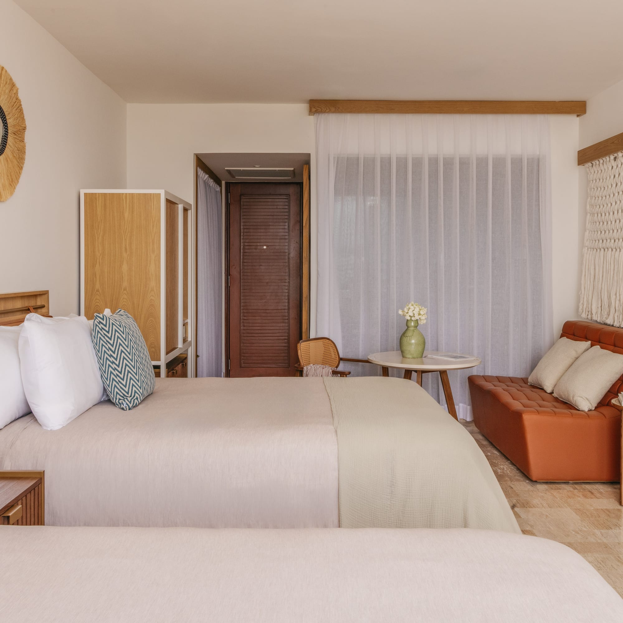 Tropical resort room with two beds, rattan mirror, orange sofa, and woven decor.