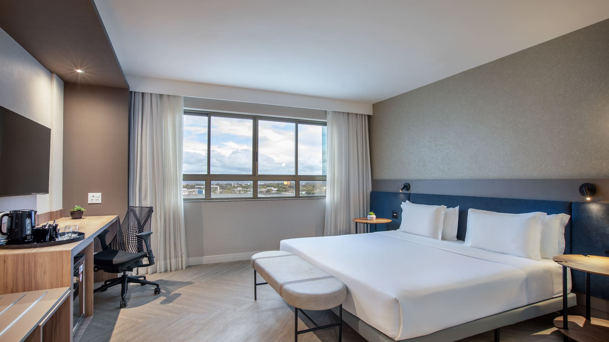 Modern hotel room with queen bed, workspace, and city view window.
