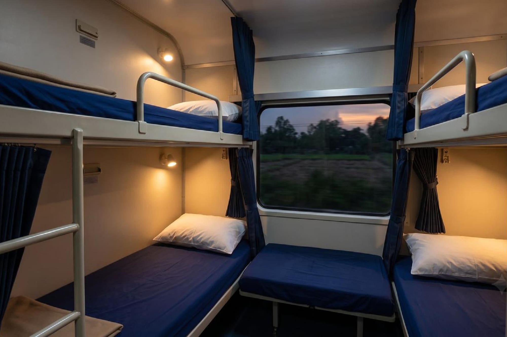 Overnight train cabin with multiple bunk beds, blue bedding, window view.