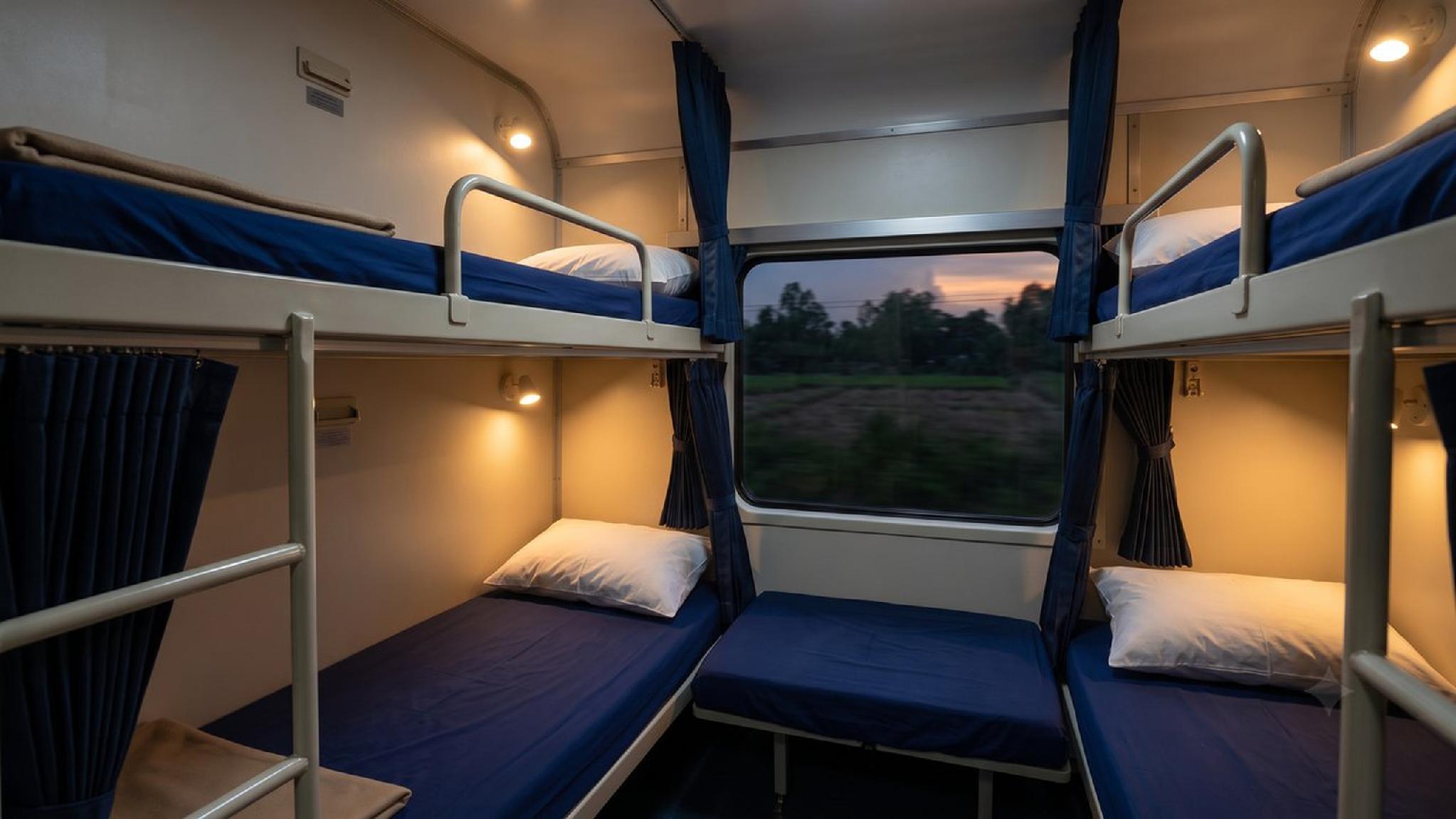 Overnight train cabin with multiple bunk beds, blue bedding, window view.