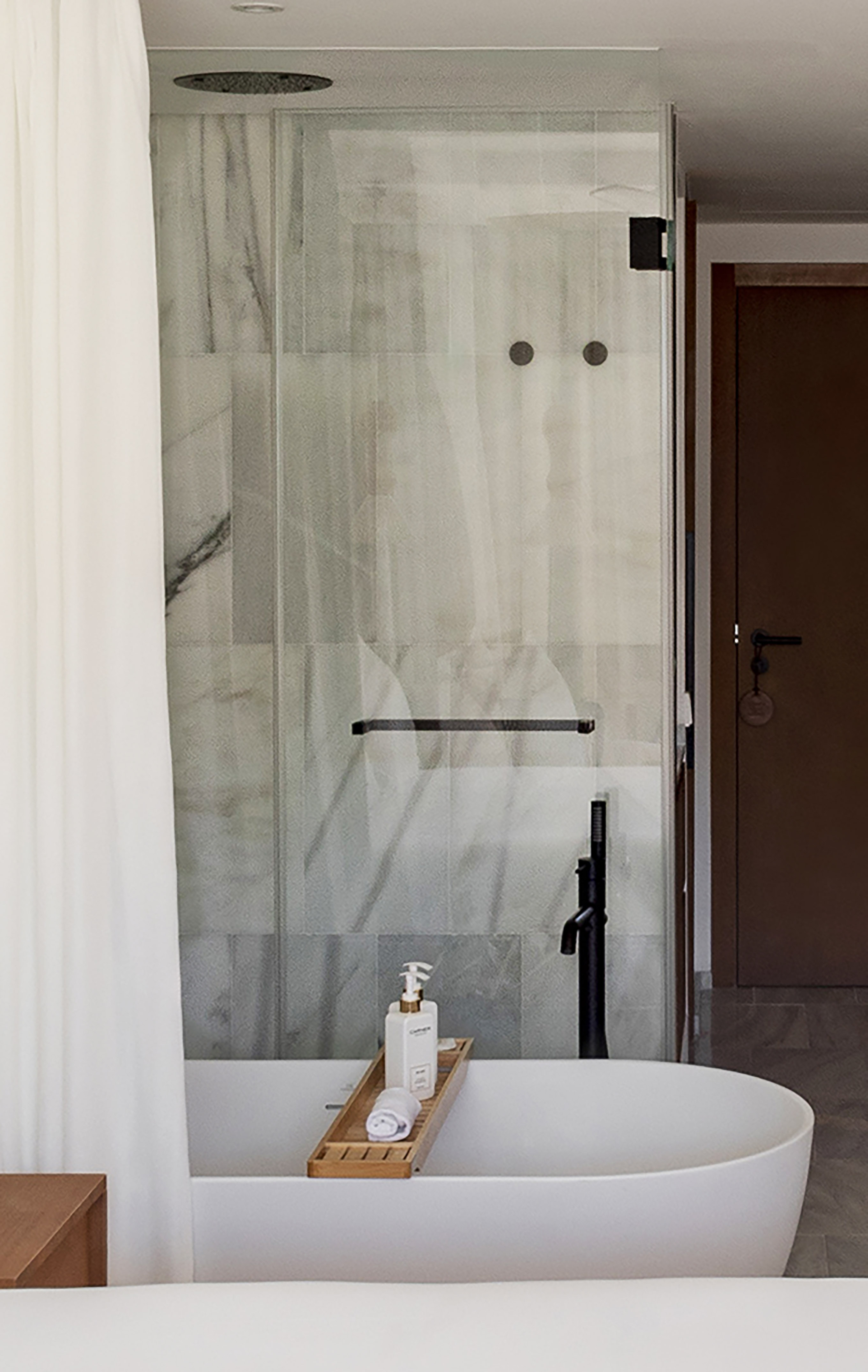 Modern bathroom: white freestanding tub, glass shower, marble wall, bath caddy.