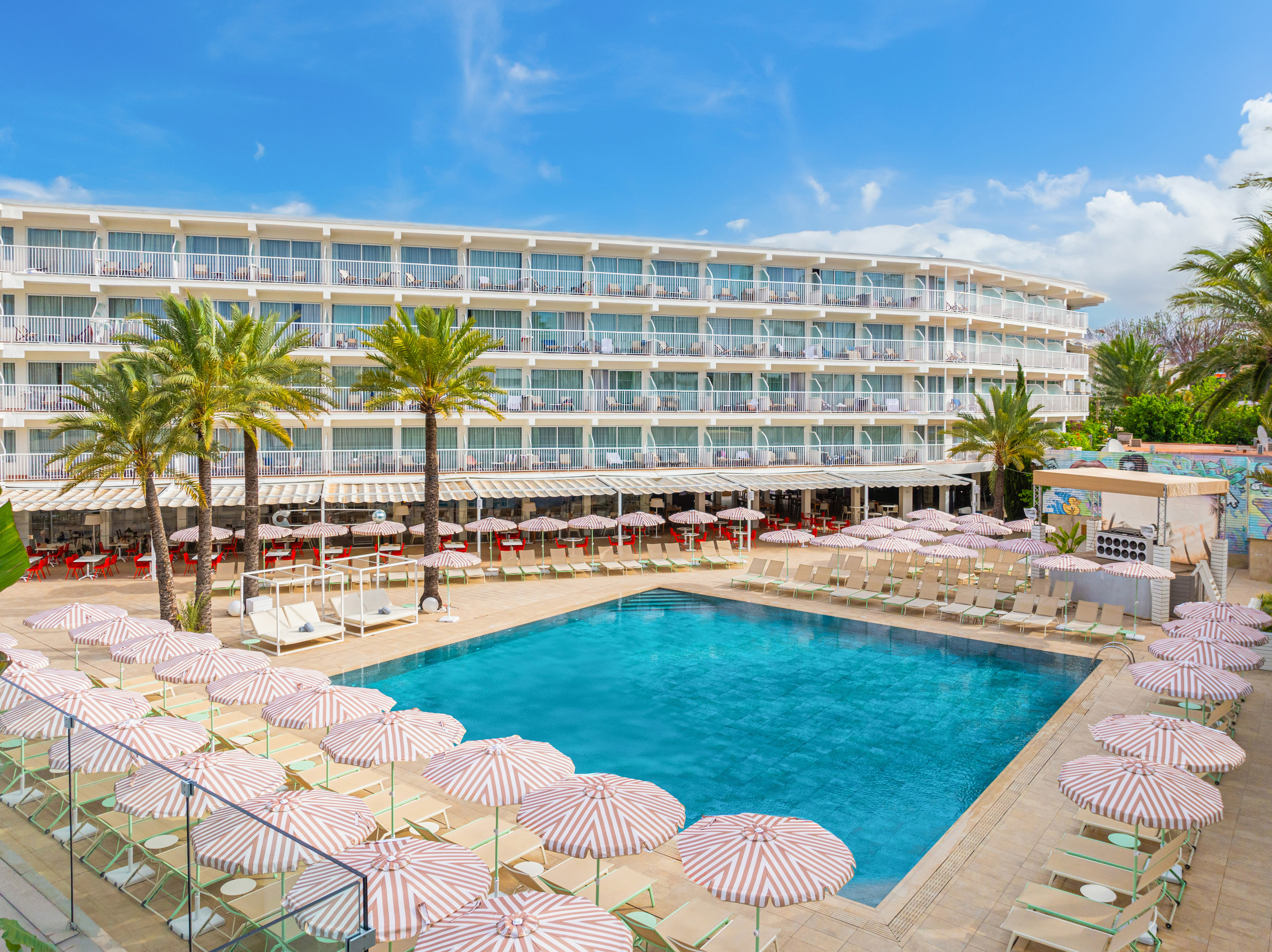 Outdoor hotel swimming pool area with palm trees and striped umbrellas.
