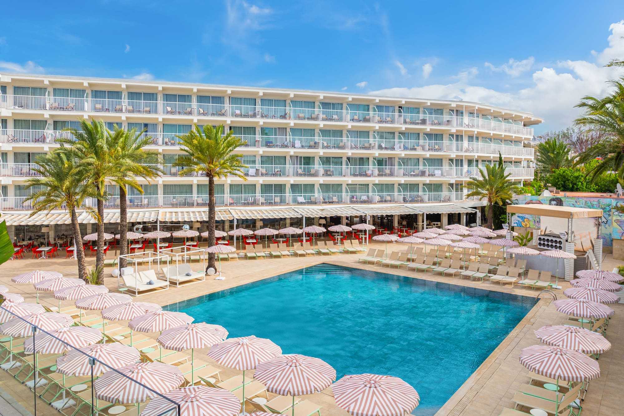 Outdoor hotel swimming pool area with palm trees and striped umbrellas.