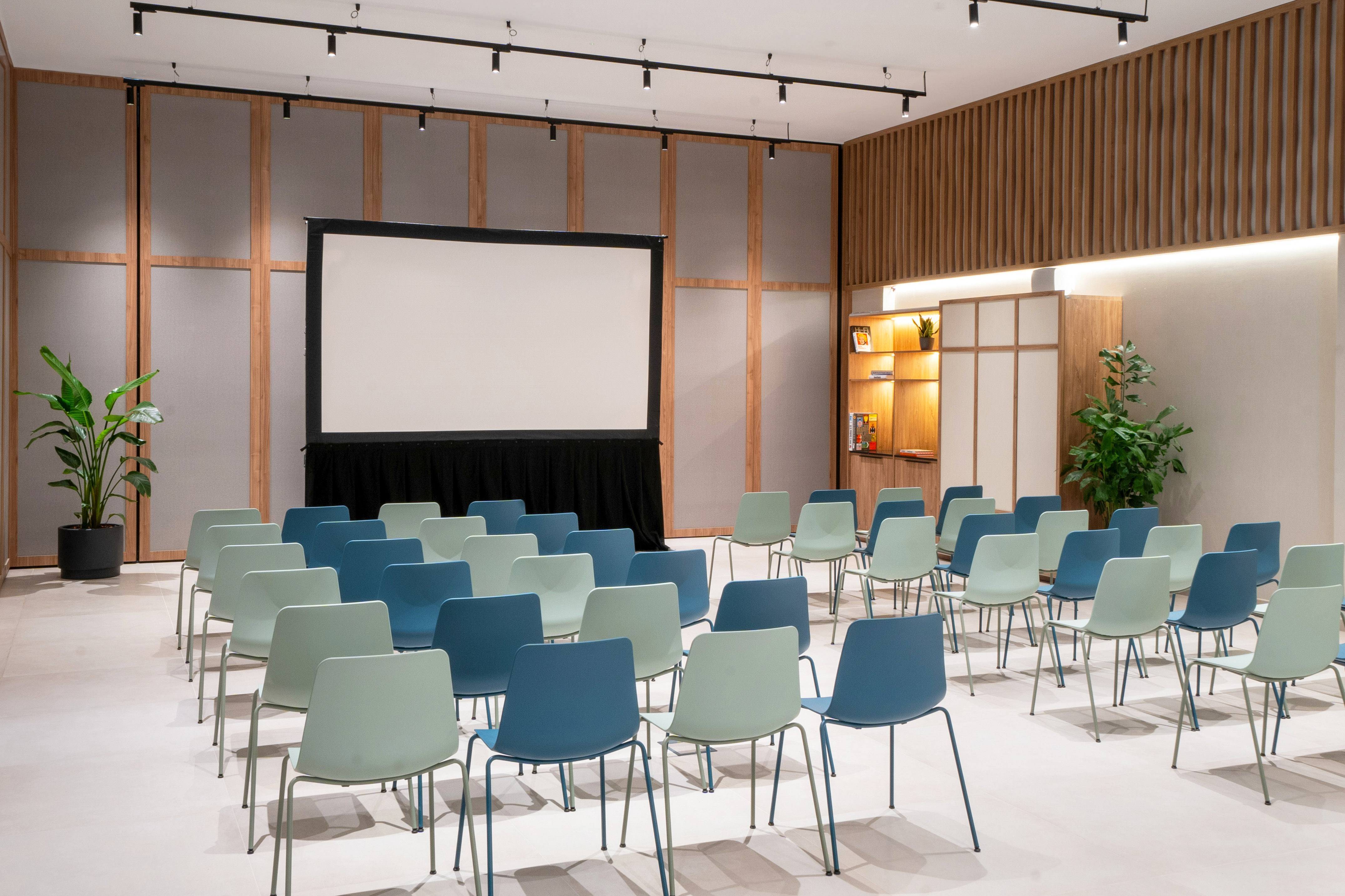 Conference room with projection screen, light blue and green chairs, wood panels.