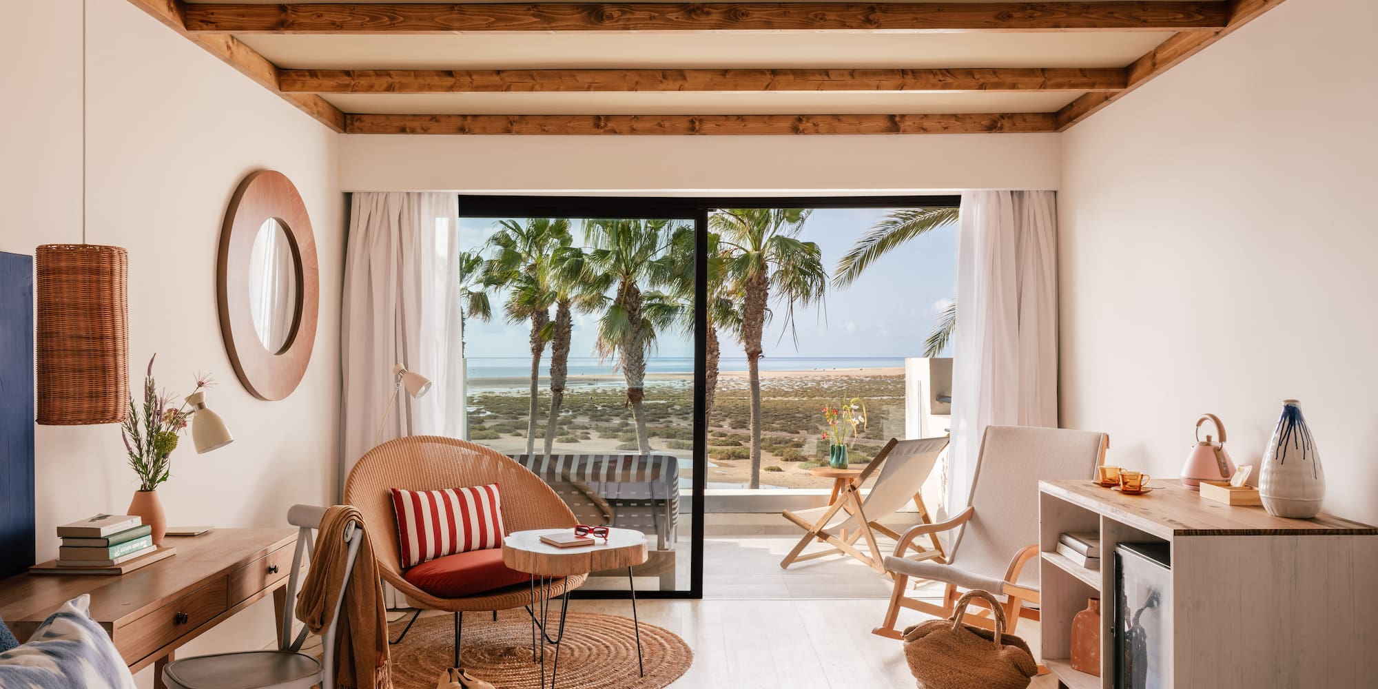 Habitación de hotel con vista al mar, palmeras y decoración costera clara.