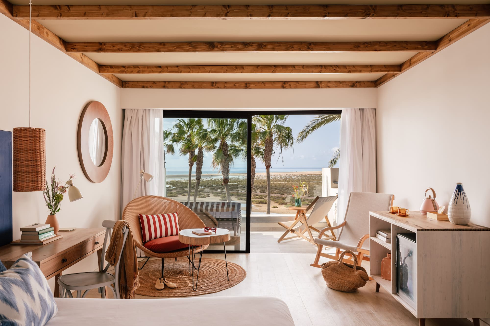 Habitación de hotel con vista al mar, palmeras y decoración costera clara.