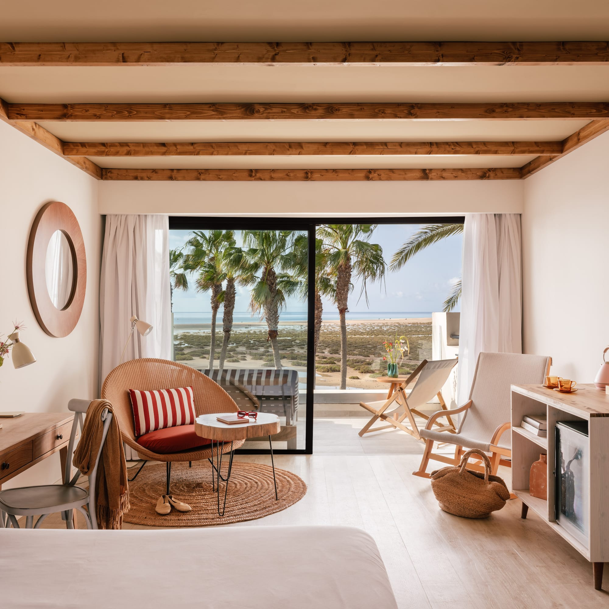 Habitación de hotel con vista al mar, palmeras y decoración costera clara.